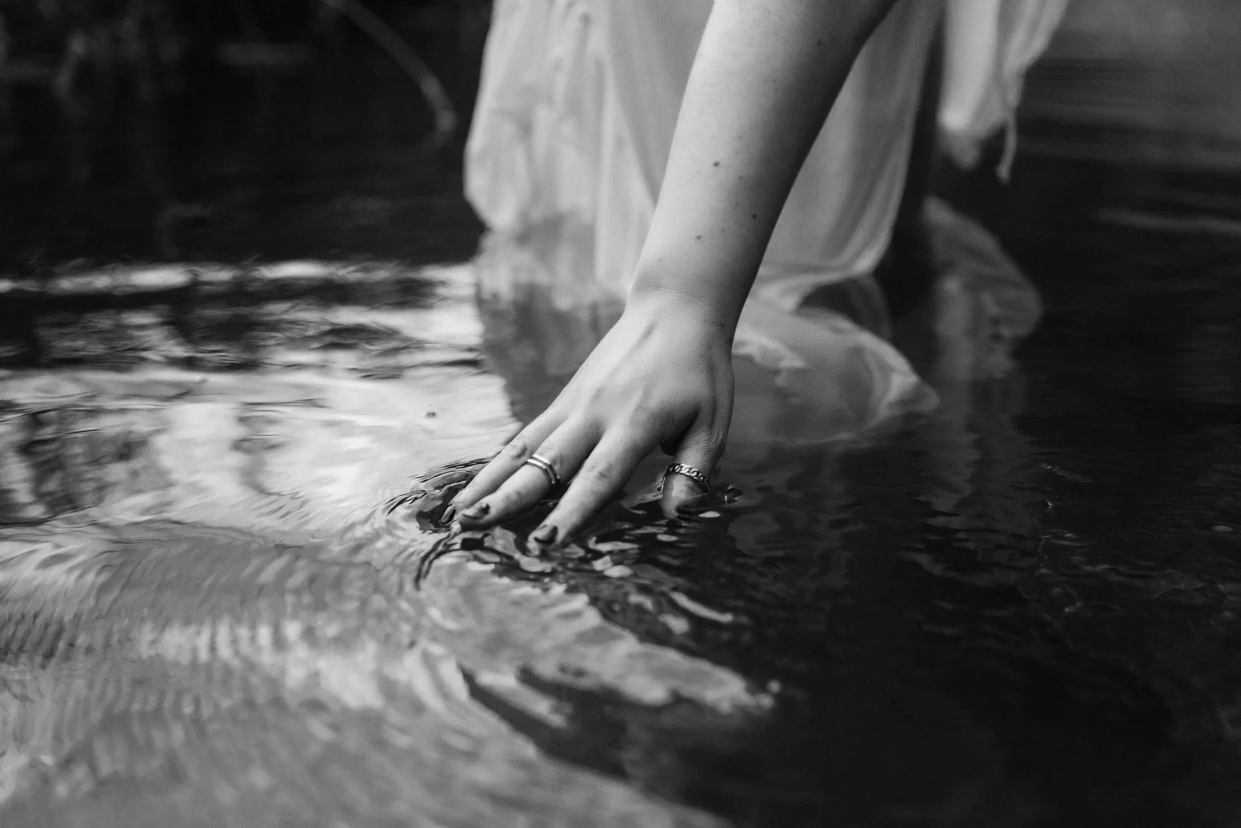 Monica Kovacs standing in water, her hand gliding across the surface, reflecting somatic, body-based sex coaching