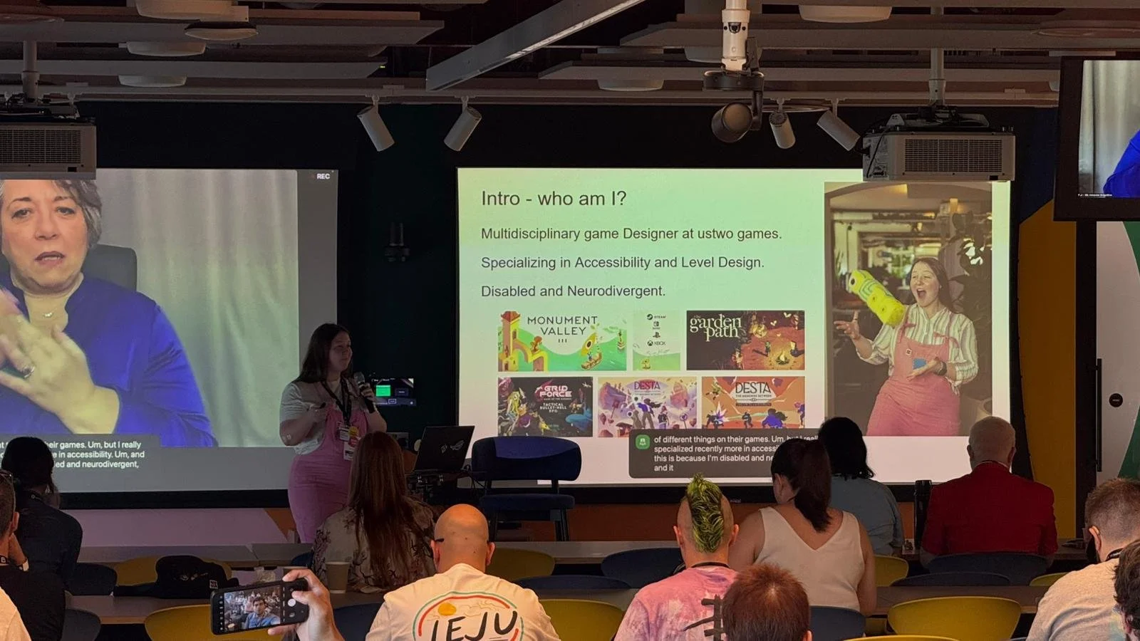 A speaker in pink dungarees presents their talk, giving an into to themselves.