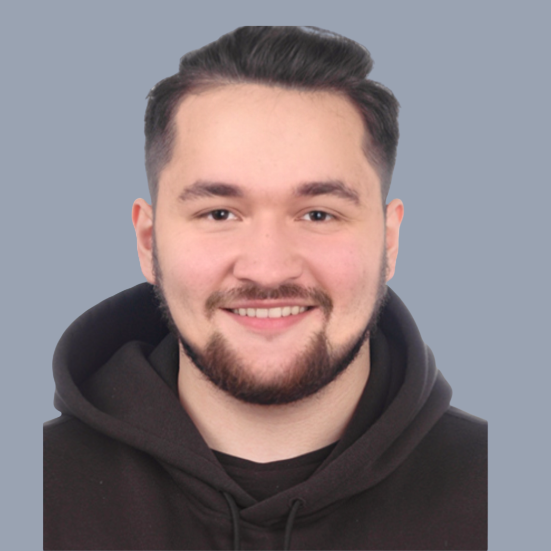 A young man with dark hair, a beard, and a big smile, wearing a black hoodie, against a plain gray background.