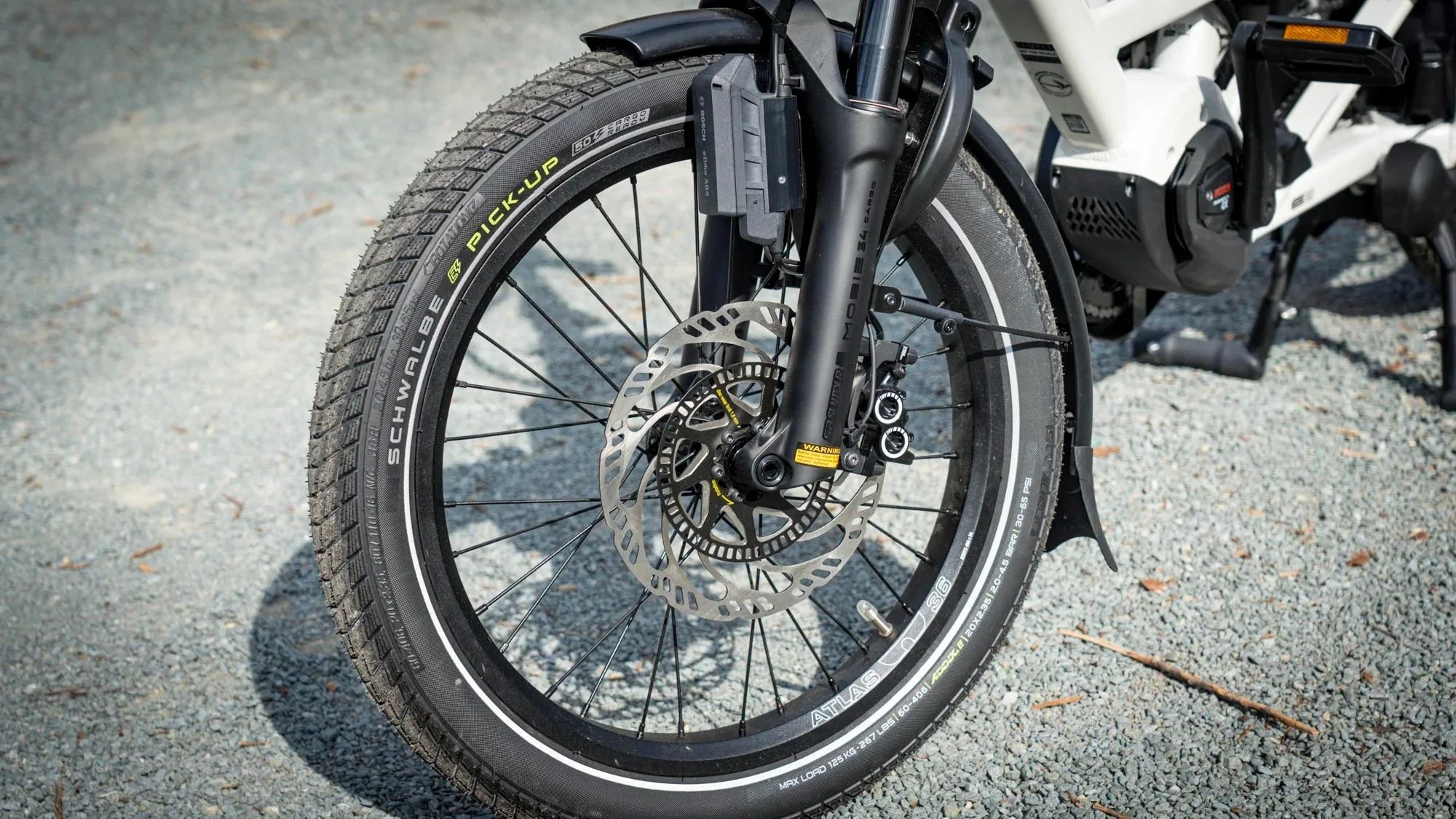 Front wheel of an electric bicycle with tubeless tire, disc brake rotor, and suspension fork on gravel ground.