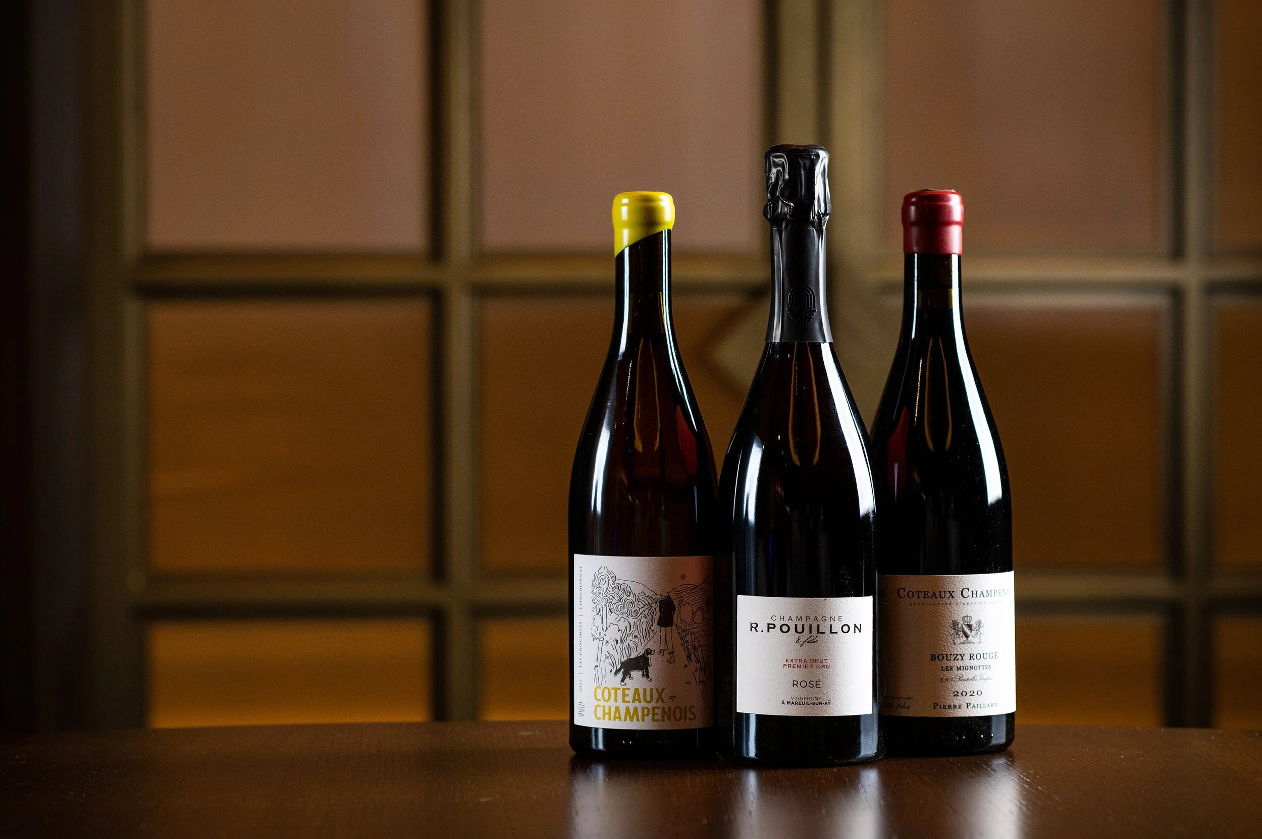 Three bottles from the Class Act Wine Club lined up in front of the brass-framed glass wall.
