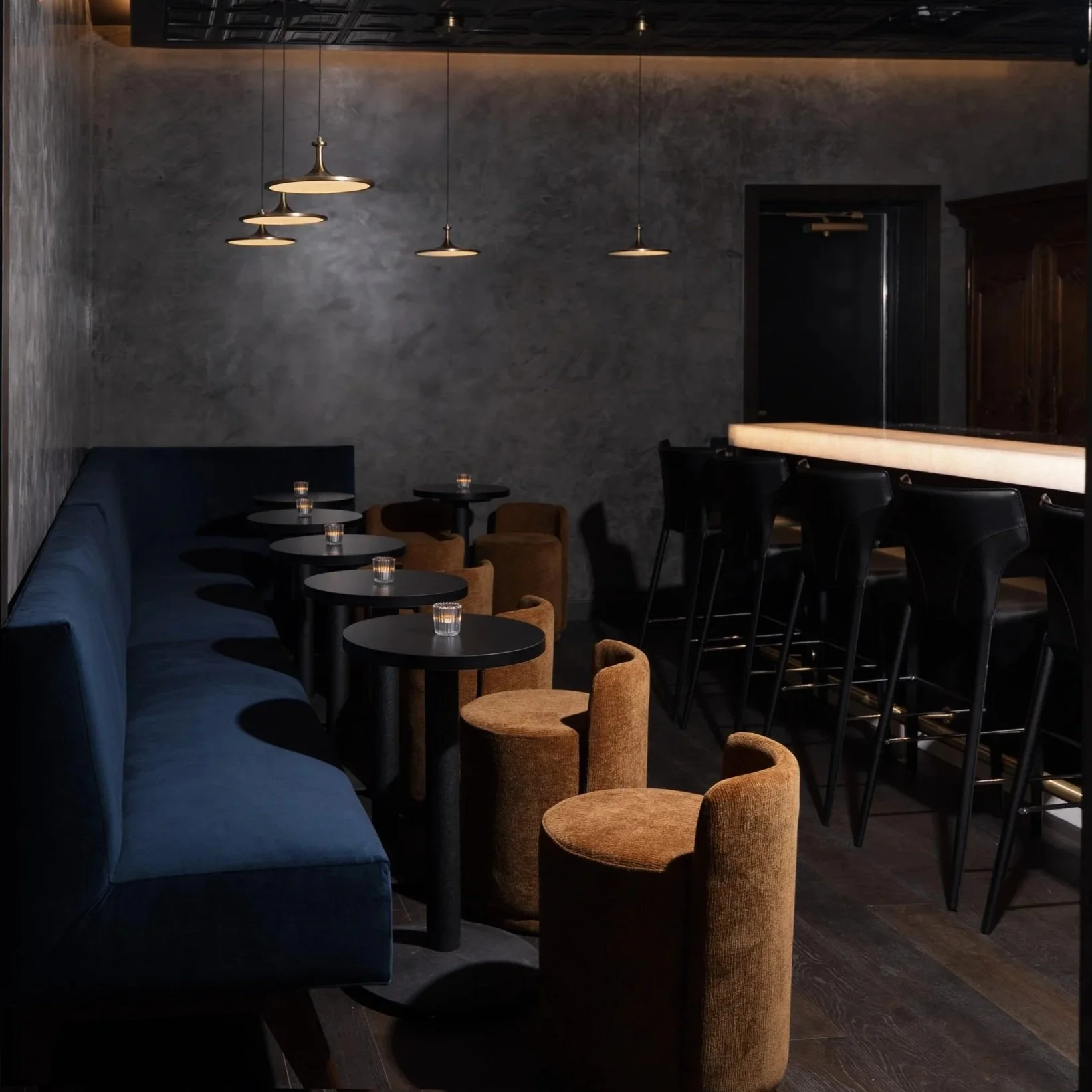 Nightcap's lounge: navy banquettes, cork stools, and the bar beneath brass pendant lights.
