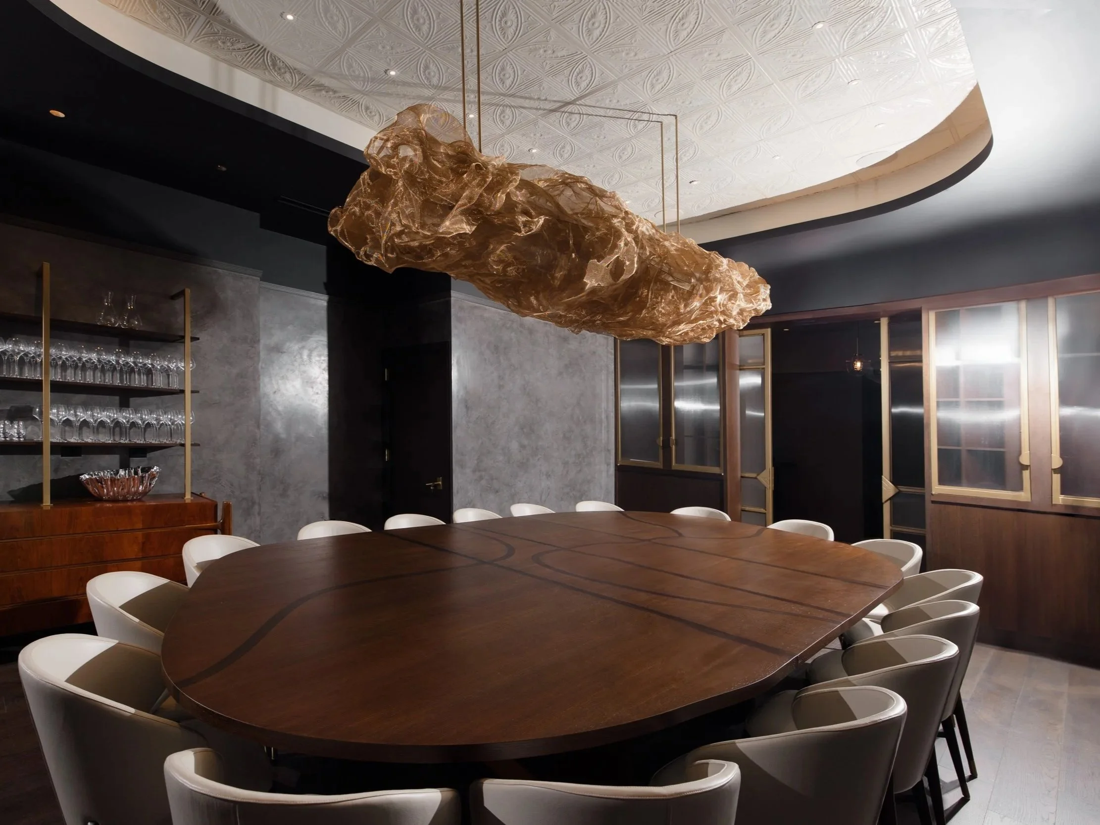 The Class Act dining room: one long table, sixteen white chairs, and the gold sculptural light above.