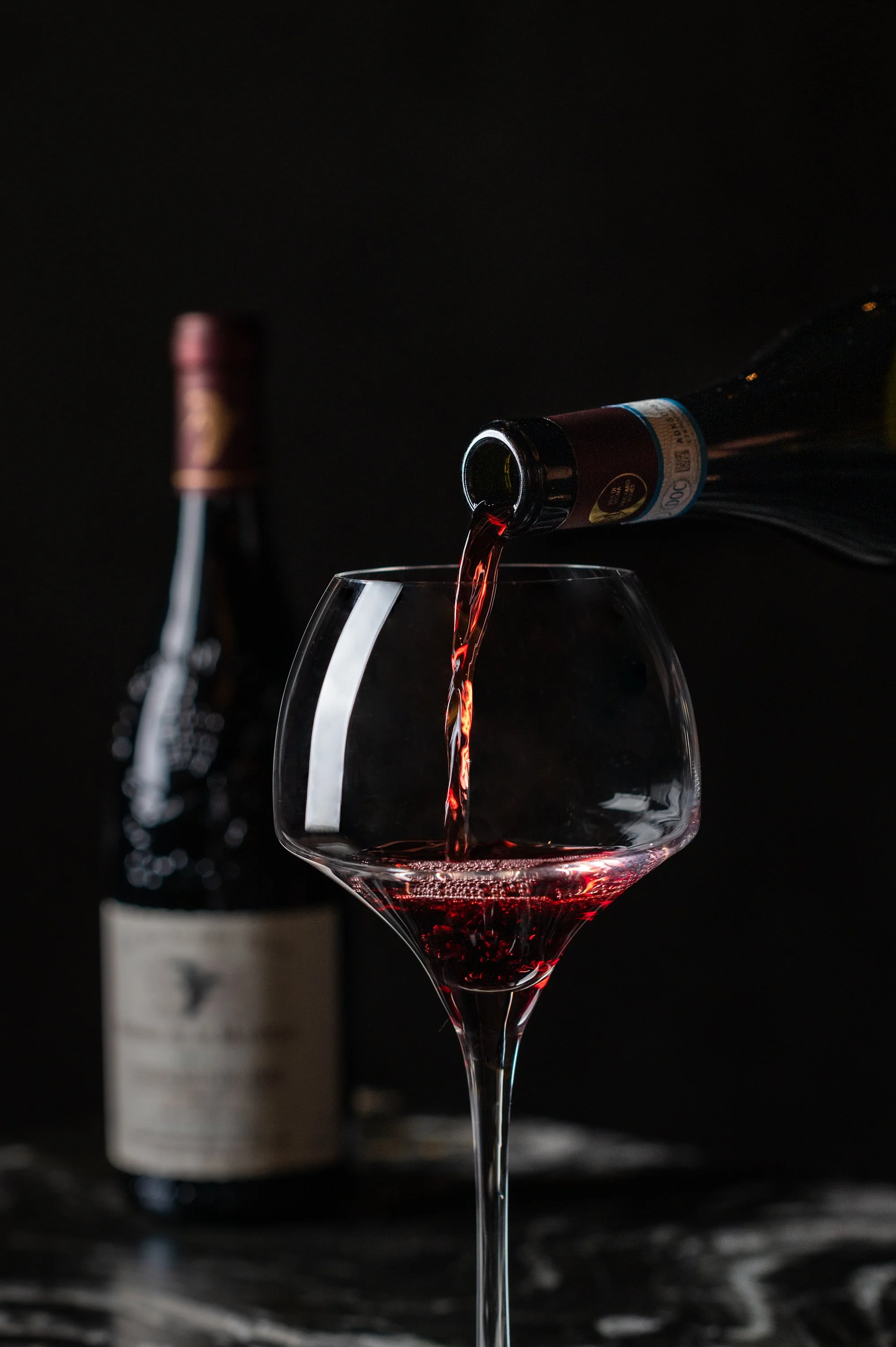 Red wine being poured into a large-bowled glass beside the bottle, for the Class Act Wine Club.