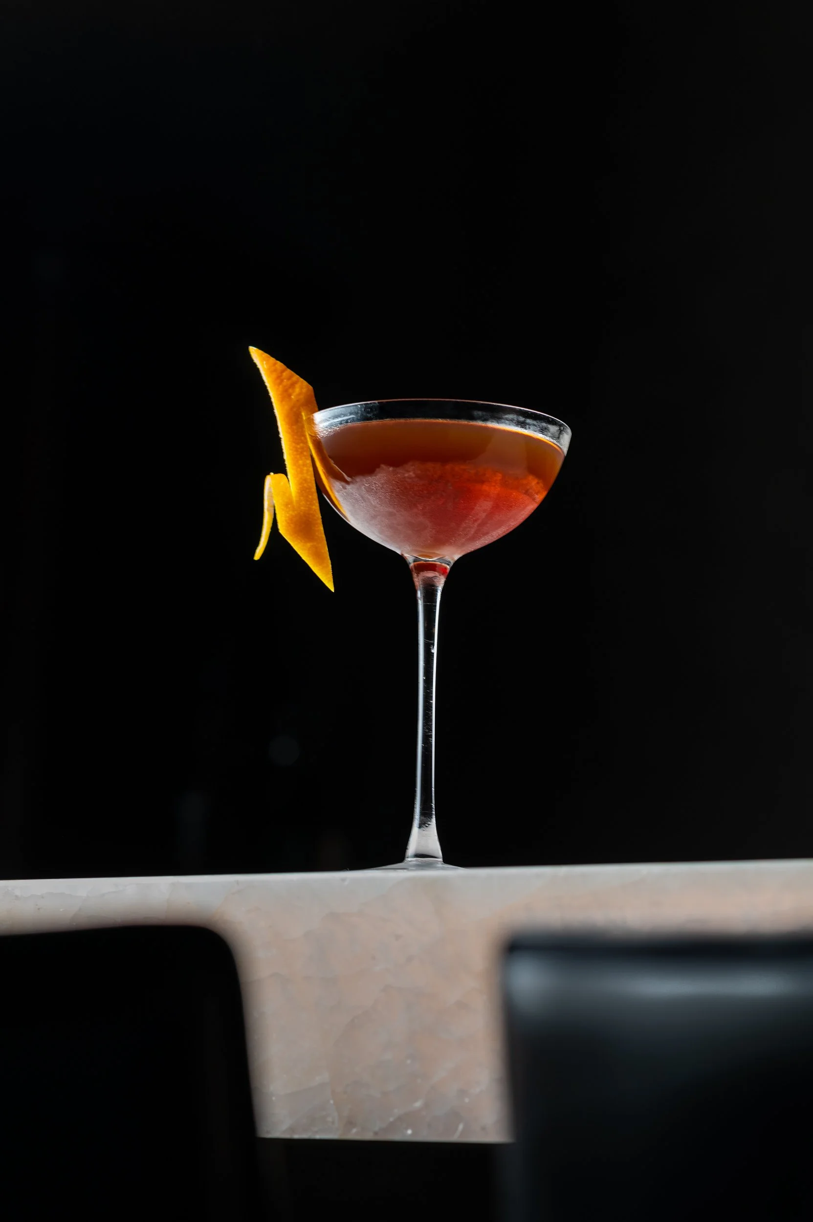 A cocktail in a coupe with a long orange twist on the marble bar at Nightcap, the speakeasy inside Class Act.