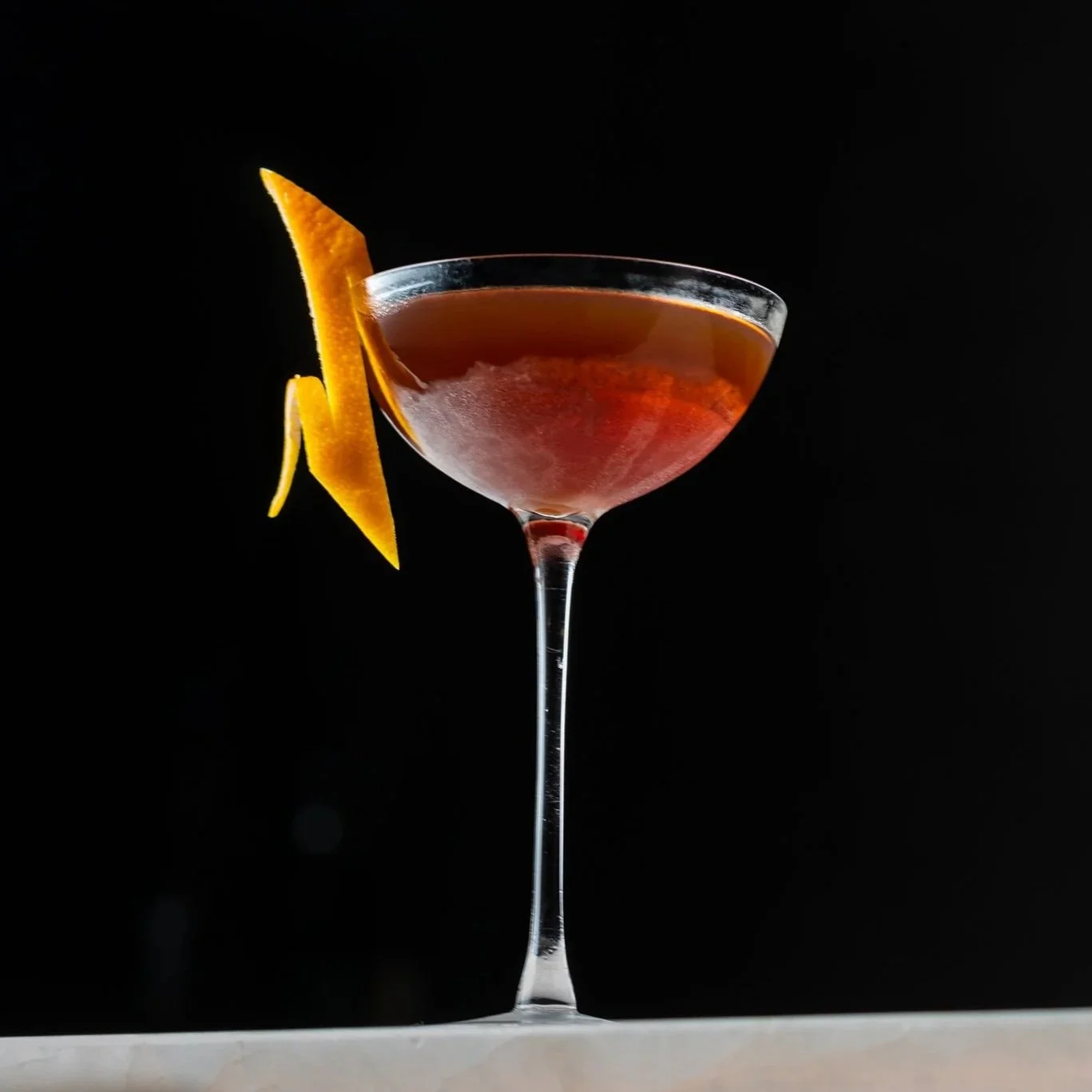 A cocktail in a coupe with a long orange twist on the marble bar at Nightcap, the speakeasy inside Class Act.