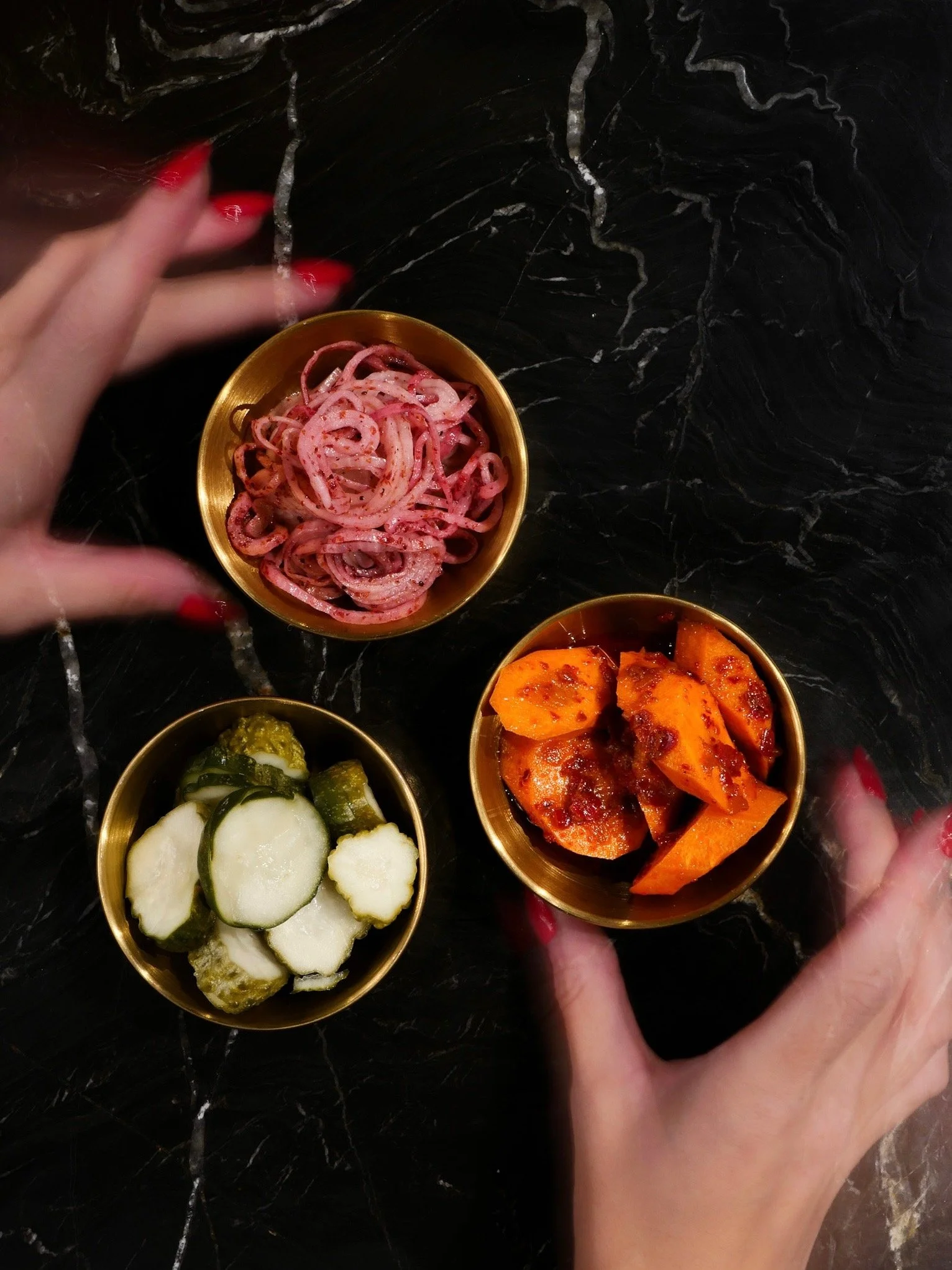 Hands reaching for small brass bowls of pickled vegetables on the marble table during Off Script, Class Act's a la carte night.