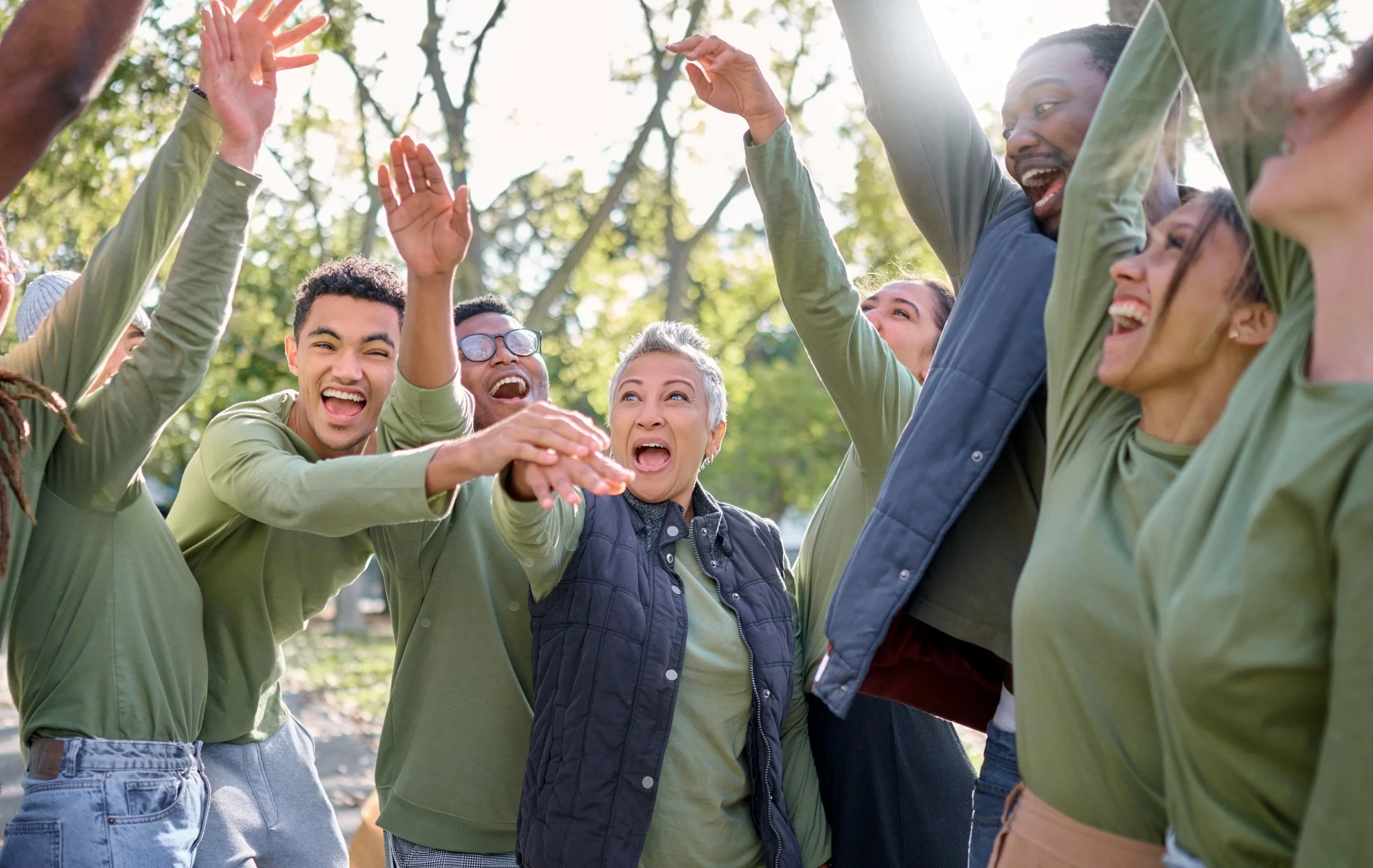 A group of diverse people outdoors celebrating with high-fives and smiles.