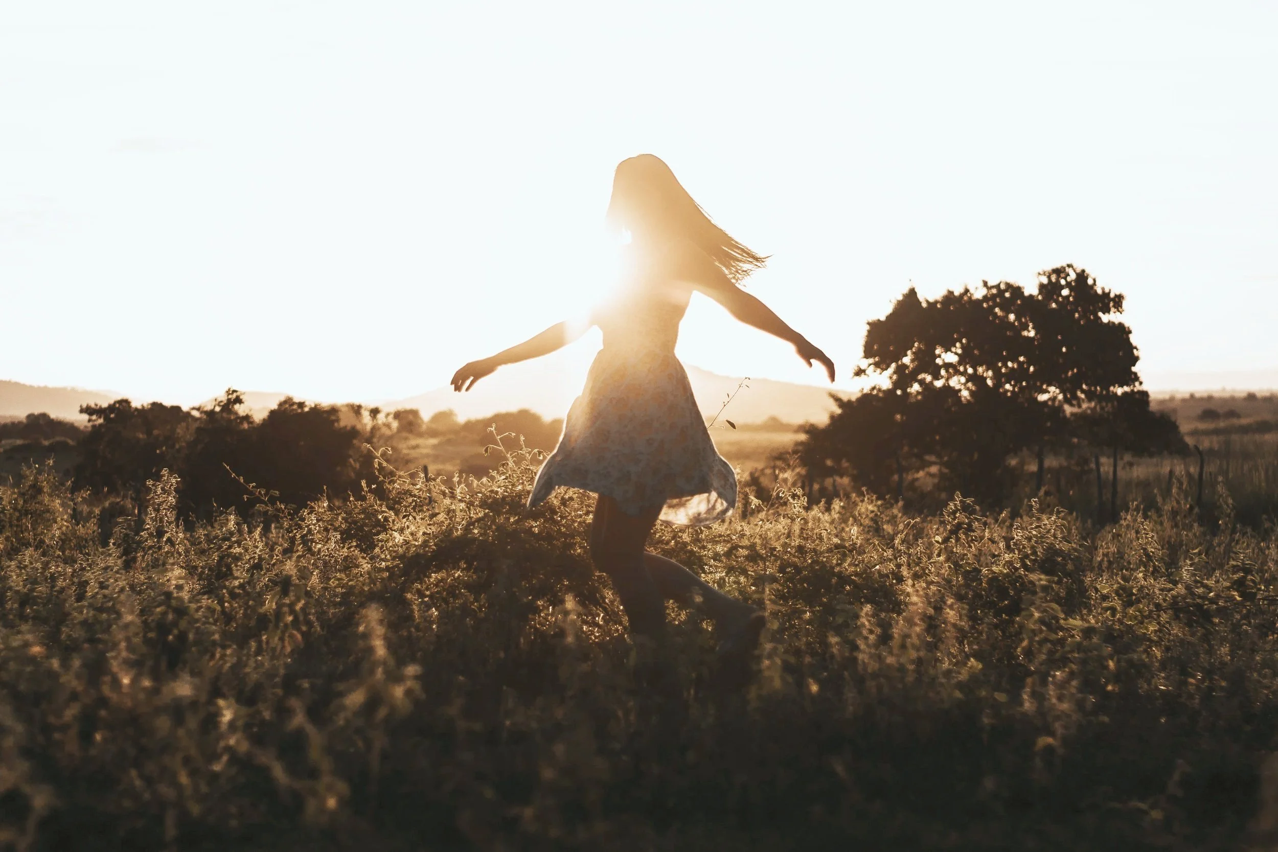Woman dancing in the sunset in a field. Approaches to therapy in Dallas, TX include Trauma Informed, Relational Therapy, with options for somatic experiencing, EMDR, and IFS.