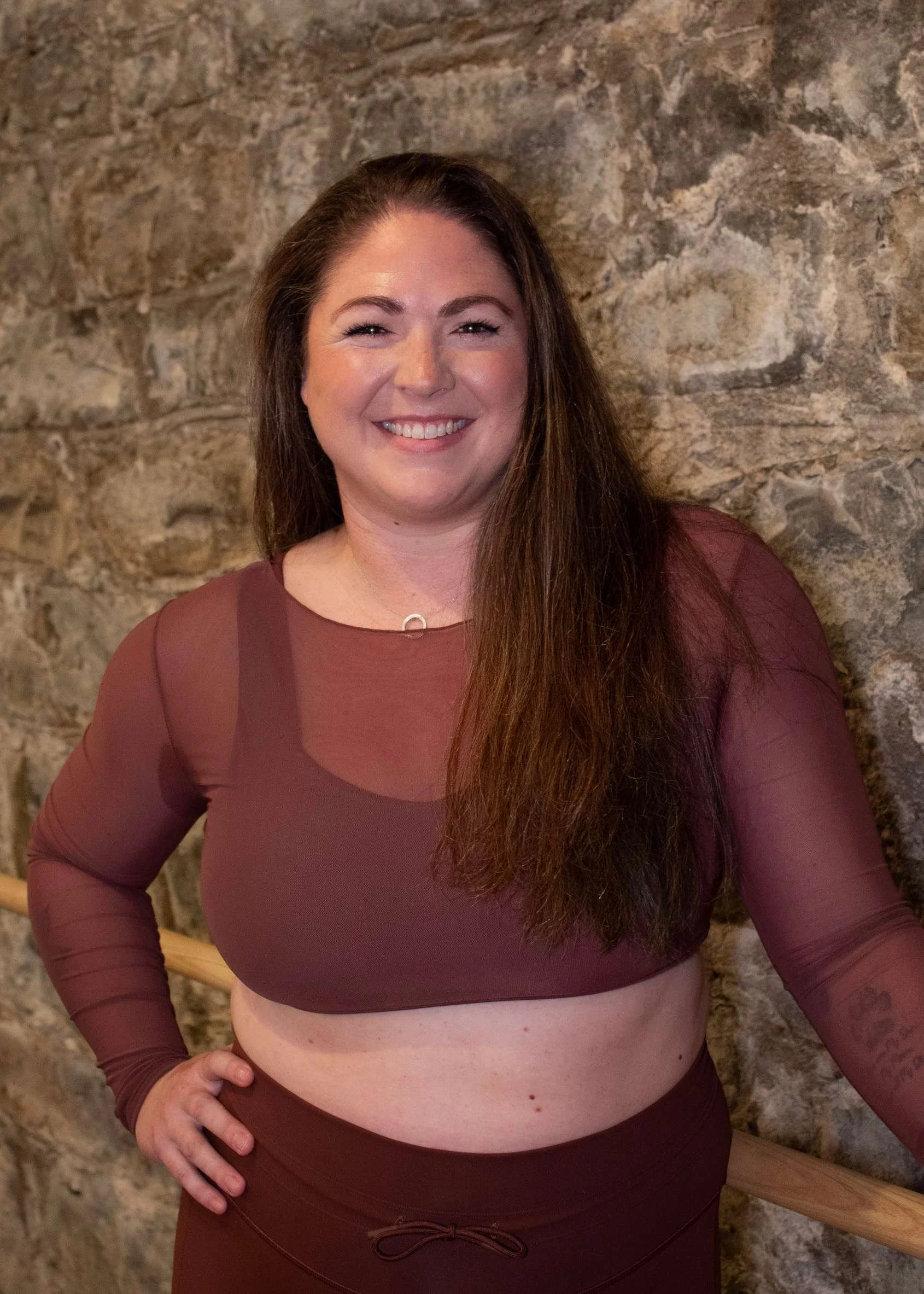 Person meditating outdoors on rocky landscape, wearing a black long-sleeve top, with eyes closed and hands resting on lap.