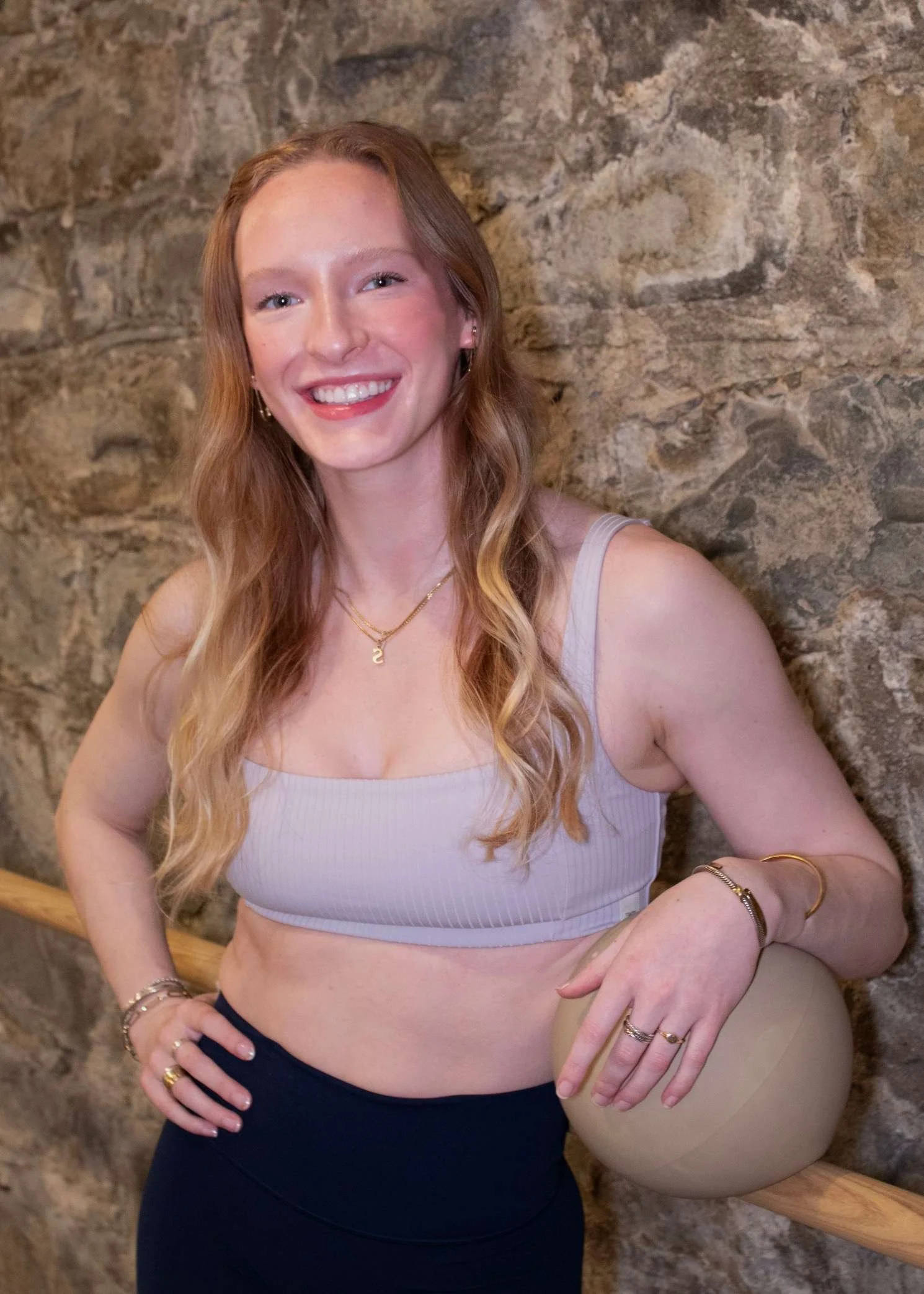 Woman in black workout outfit sitting on a yoga mat, smiling.