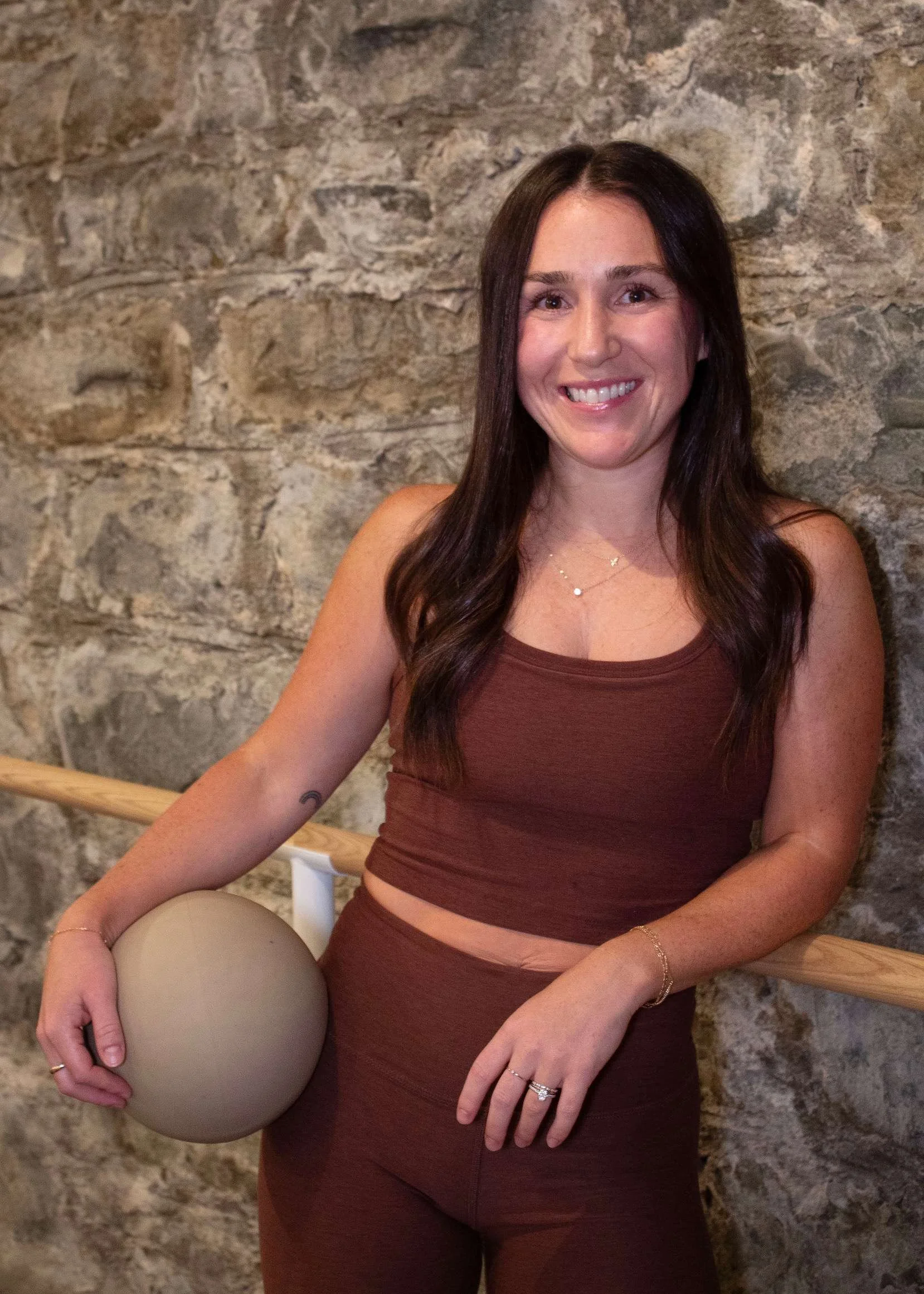Woman in blue workout outfit smiling in a fitness studio with wavy wall decor and neon signs that read 'together we Rise' and 'together we are' in the background.