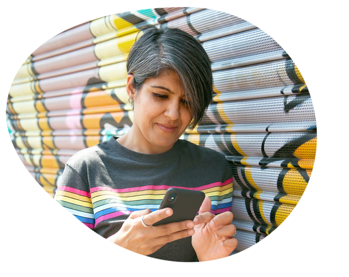 Image shows a woman standing against a metal door. She's looking down at her phone.
