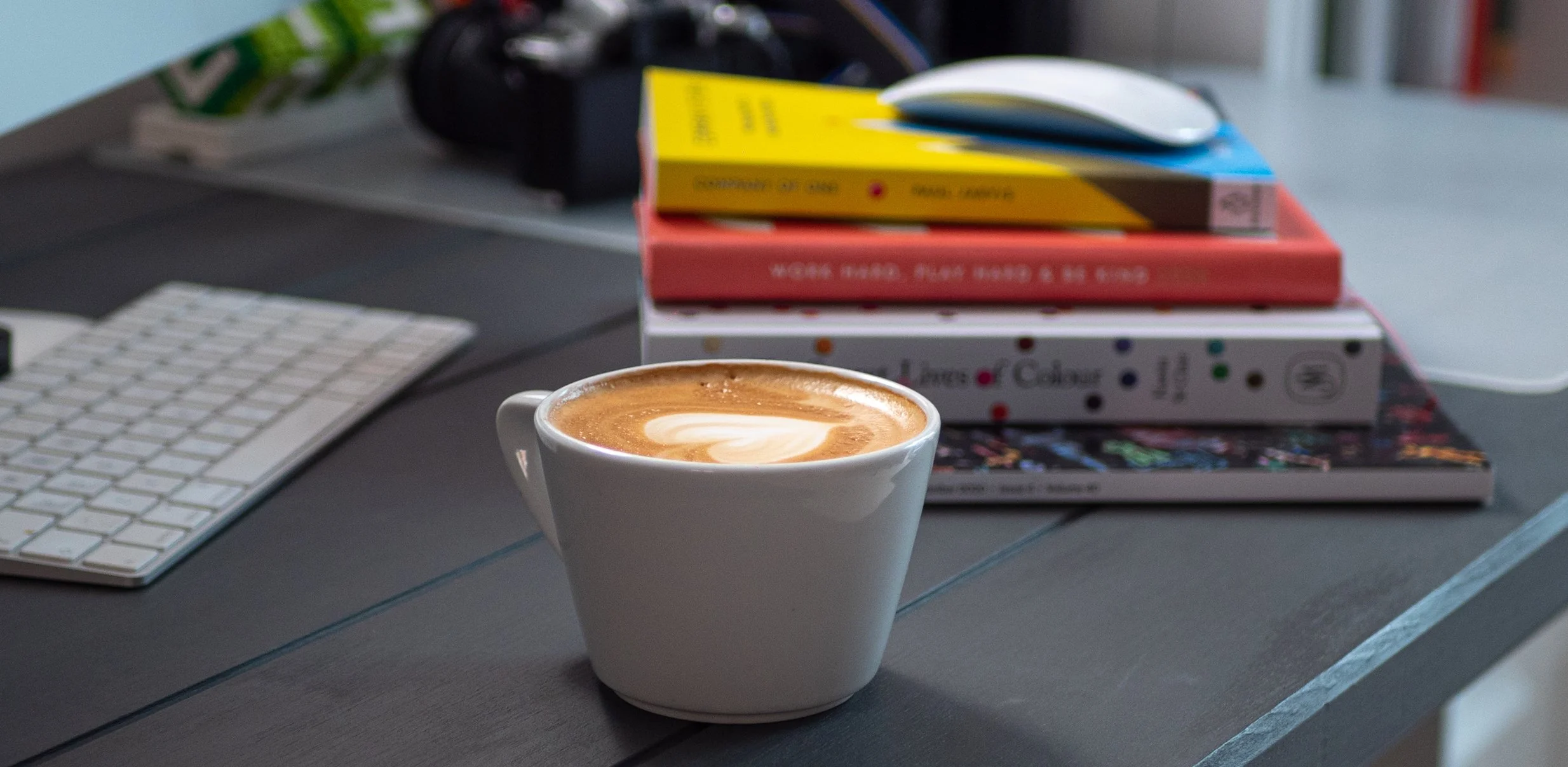 A coffee cup on a desk with design books and a keyboard