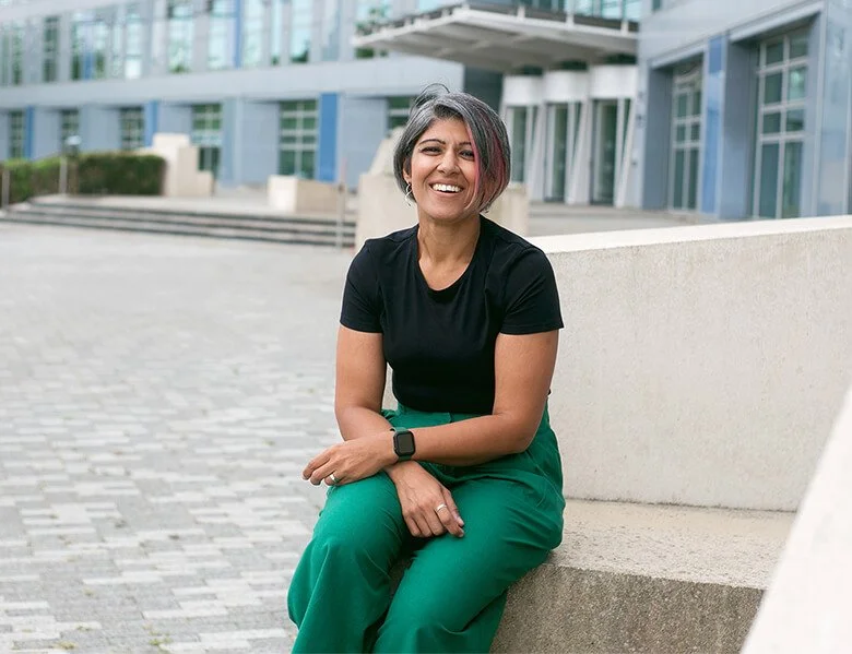 Image shows a woman sitting on a step. She's wearing green trousers and a black tshirt.