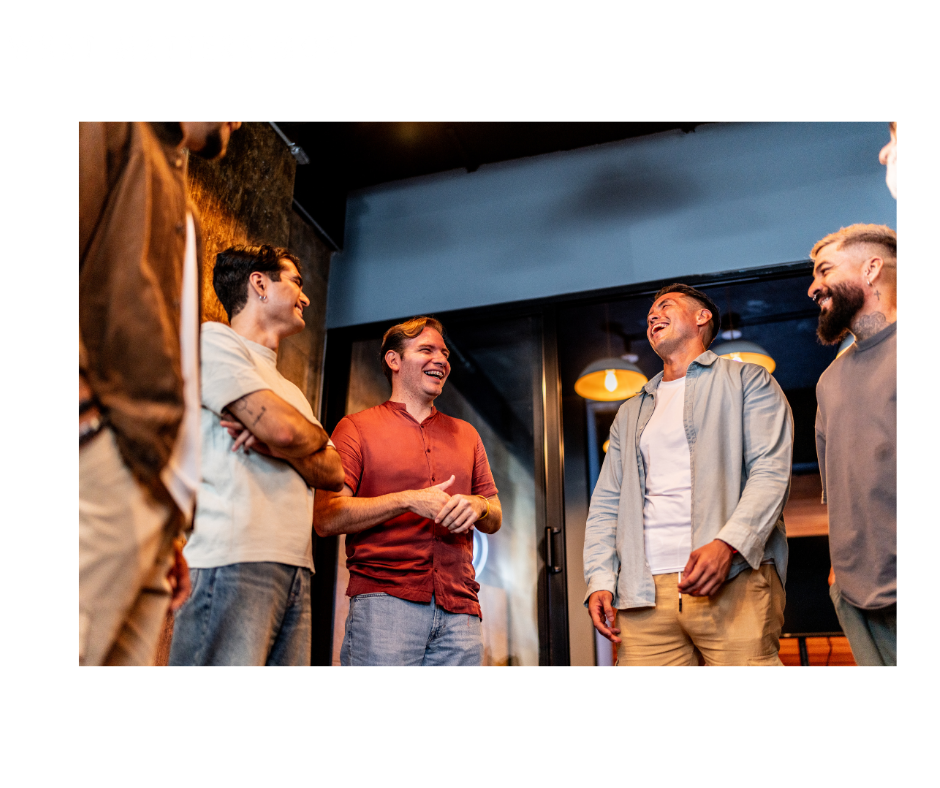 Group of five men casually talking and laughing indoors, possibly in a restaurant or bar setting.