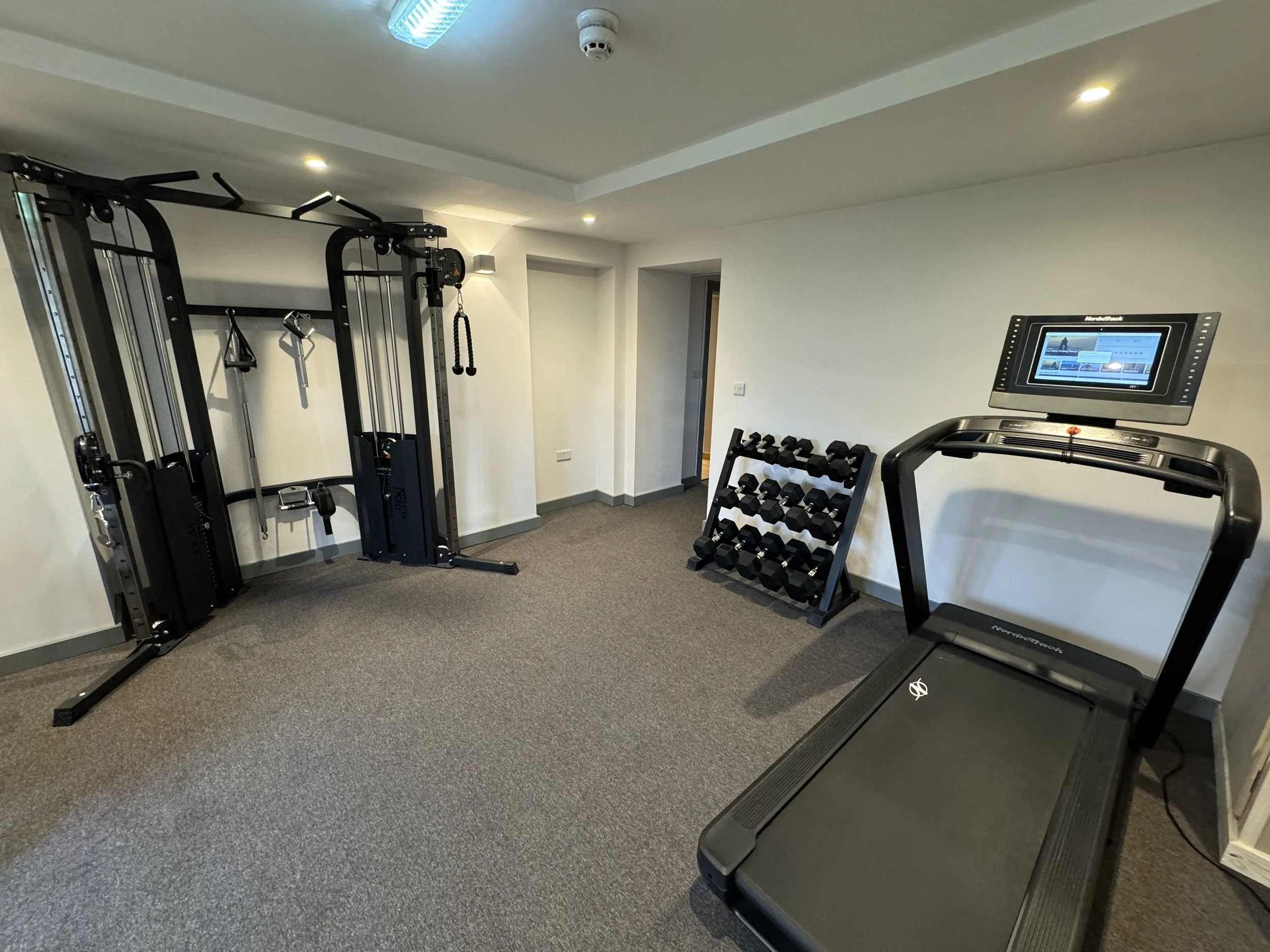Empty home gym with a weight machine, a set of dumbbells on a rack, and a treadmill with a digital display.