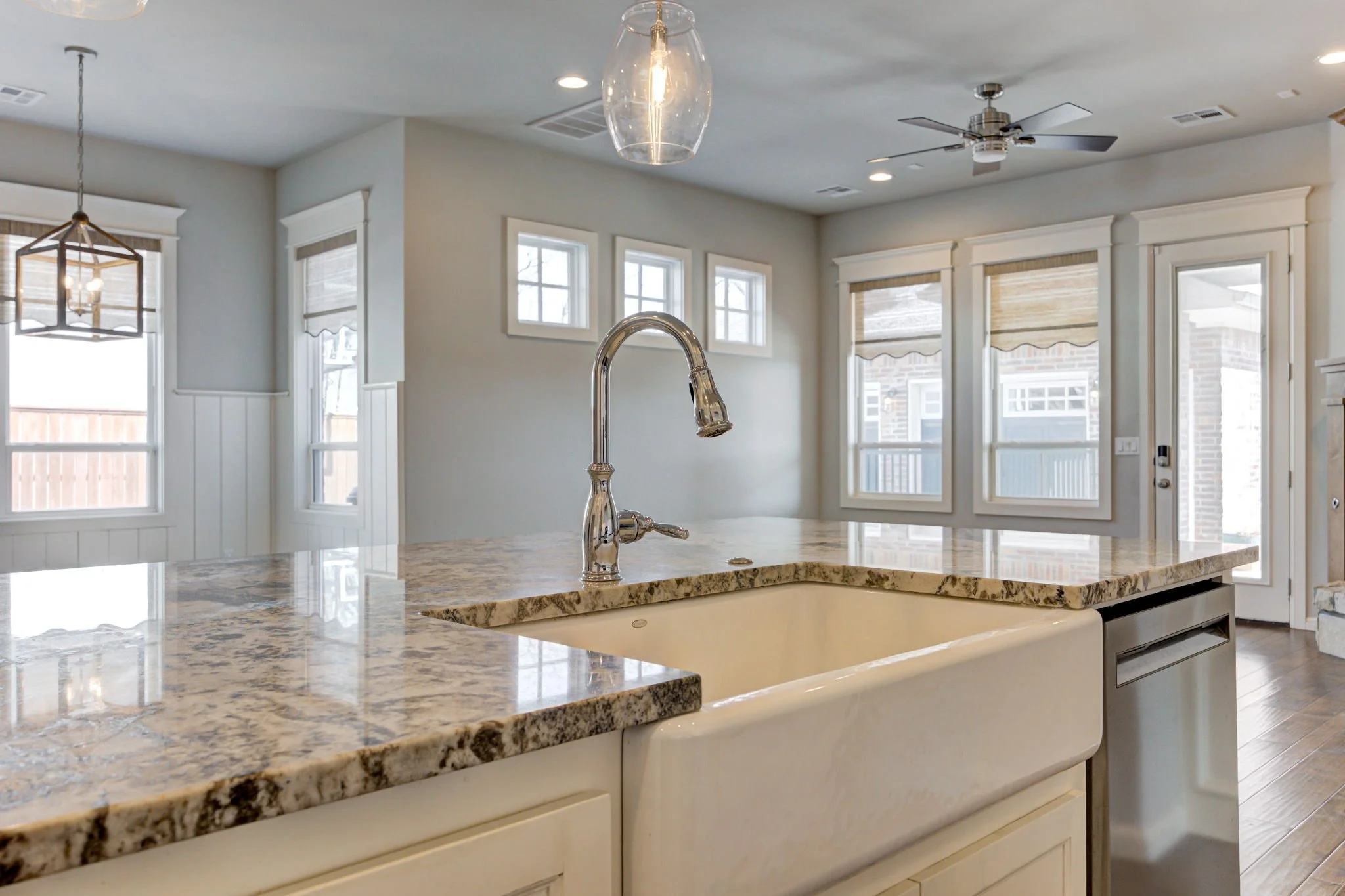 Modern kitchen with granite countertops, white cabinets, a farm-style sink, and windows with beige Roman shades.