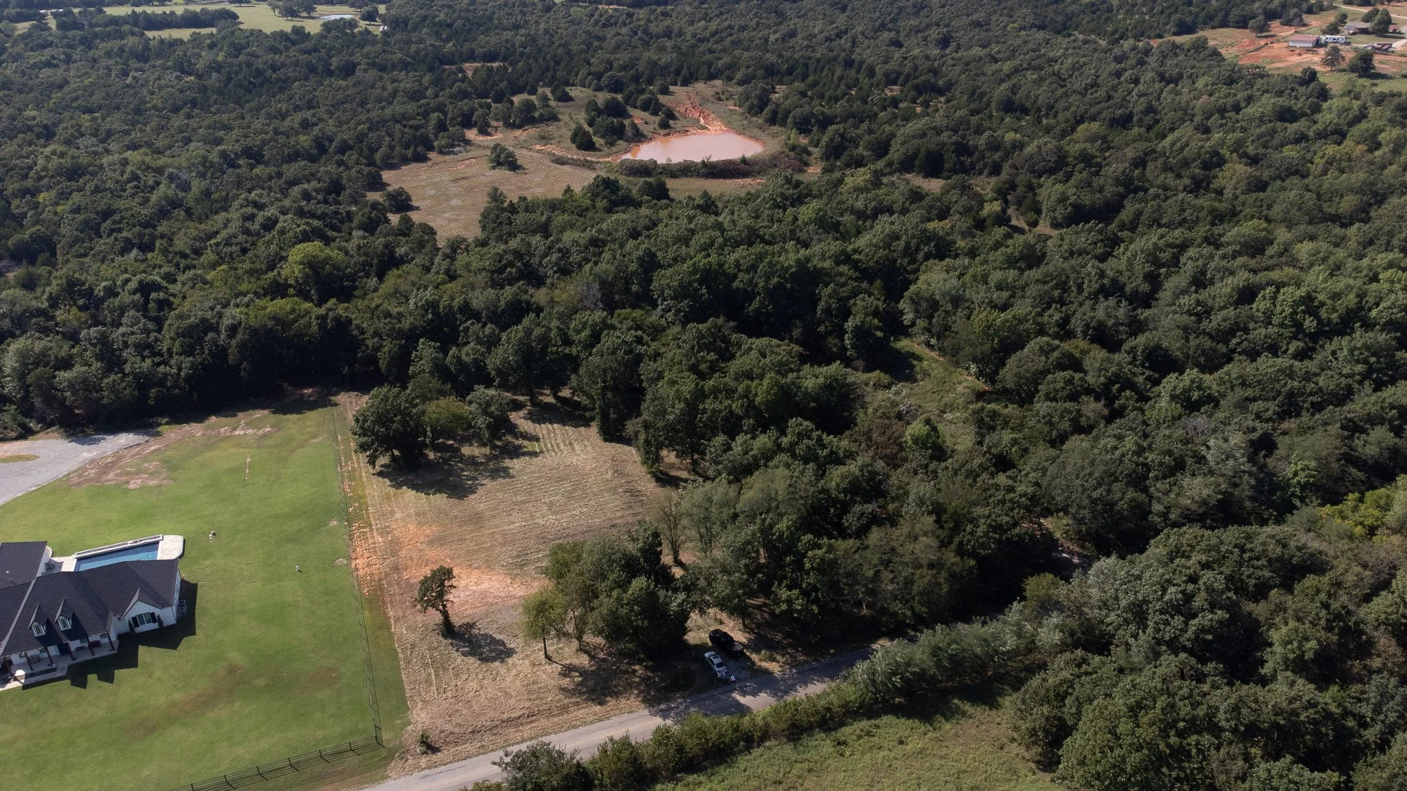 An elevated drone shot capturing a 10-acre lot featuring a cleared building site and lush, mature timber. This property offers the perfect balance of open space and forest, ideal for a custom rural estate in Eastern Oklahoma County.