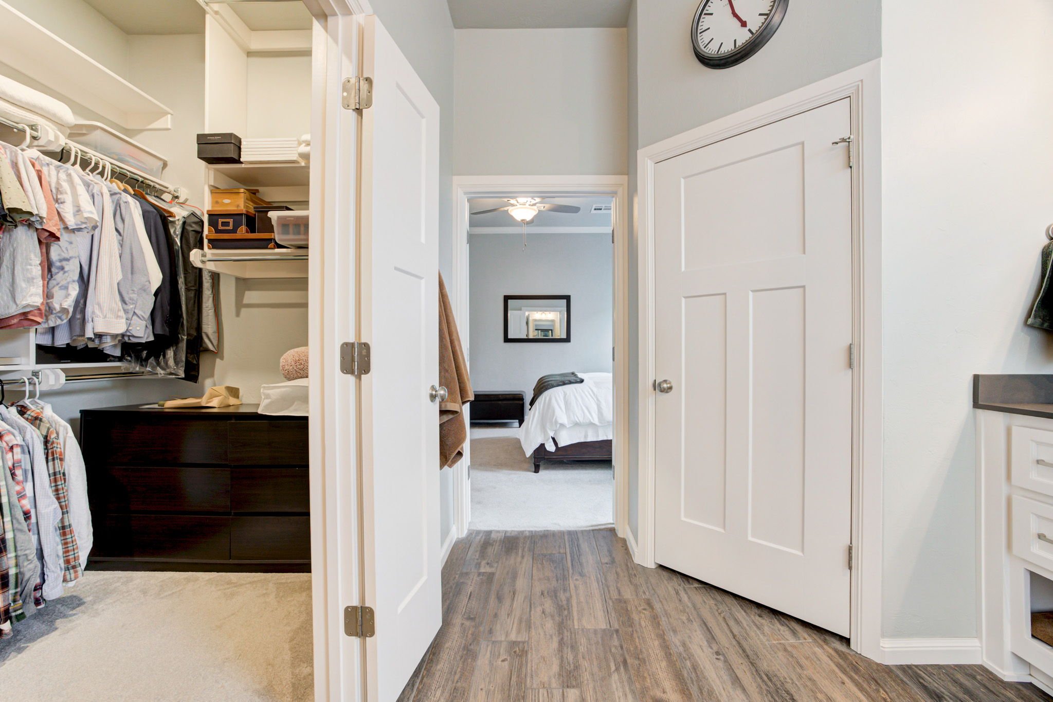 A view of a hallway leading to a bedroom with a bed, another open closet, and neutral-colored walls.