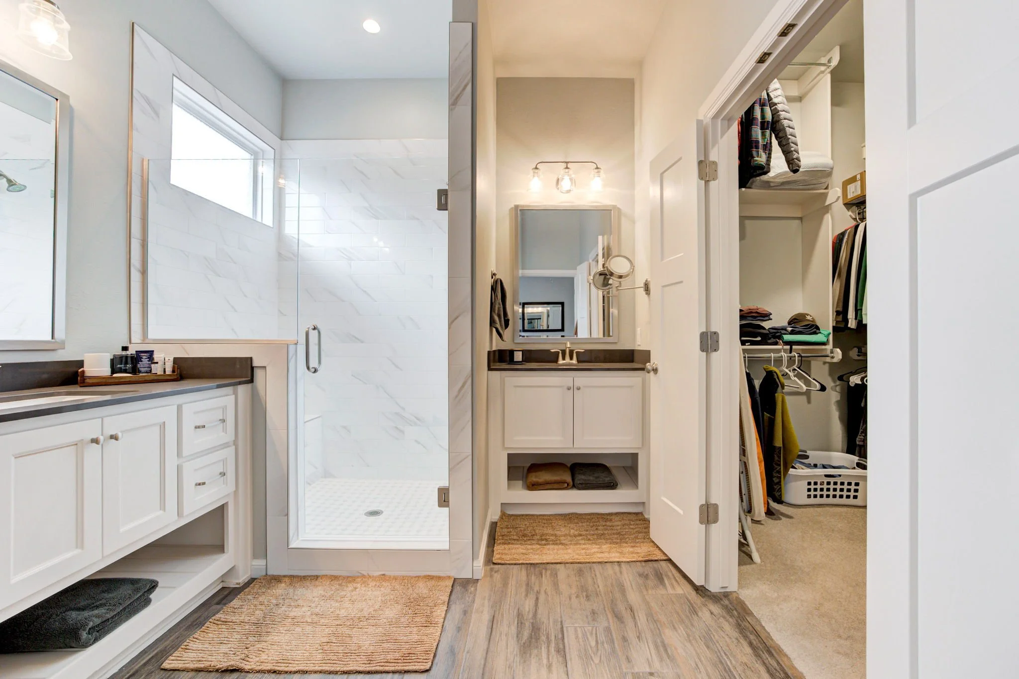 Bathroom with shower, vanity, mirror, and open walk-in closet filled with clothes and towels.