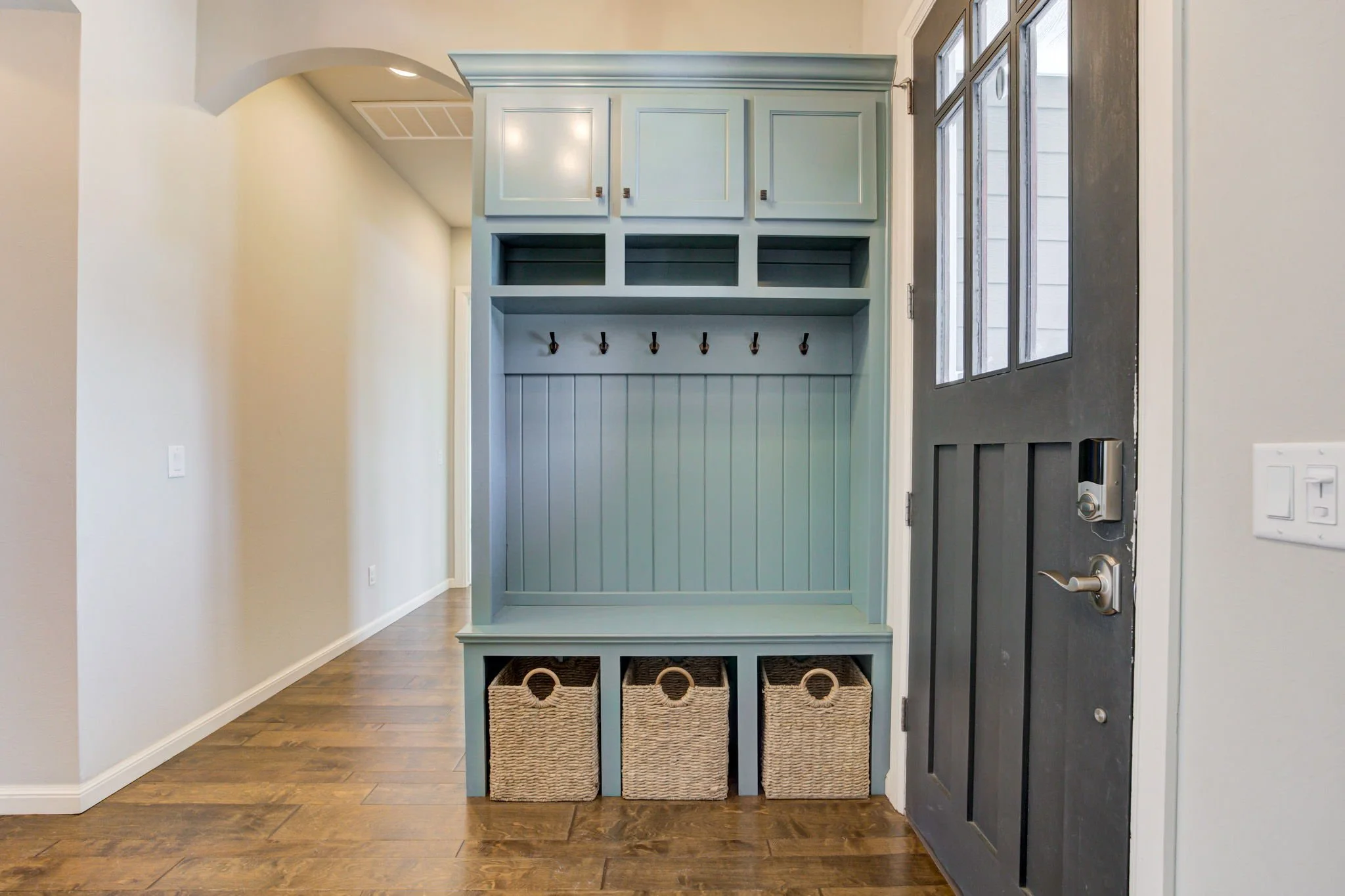 Entryway storage unit with cubbies, hooks, and baskets next to a black door with windows.