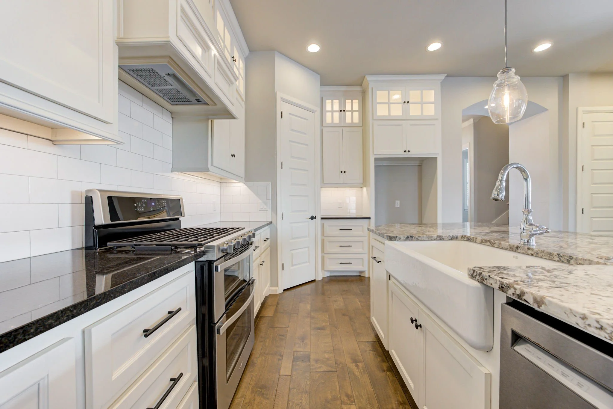 Bright modern kitchen with white cabinets, granite countertops, wood flooring, stainless steel appliances, white subway tile backsplash, and pendant lighting.