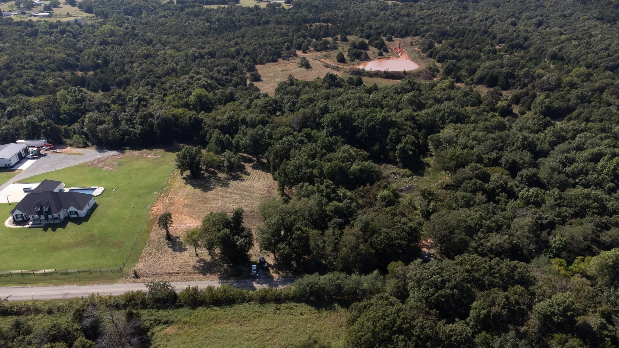 This shot provides a clear view of the paved road access for this 10-acre lot. The image emphasizes the deep lot lines and the significant timber value, showcasing a prime piece of Jones real estate ready for development.