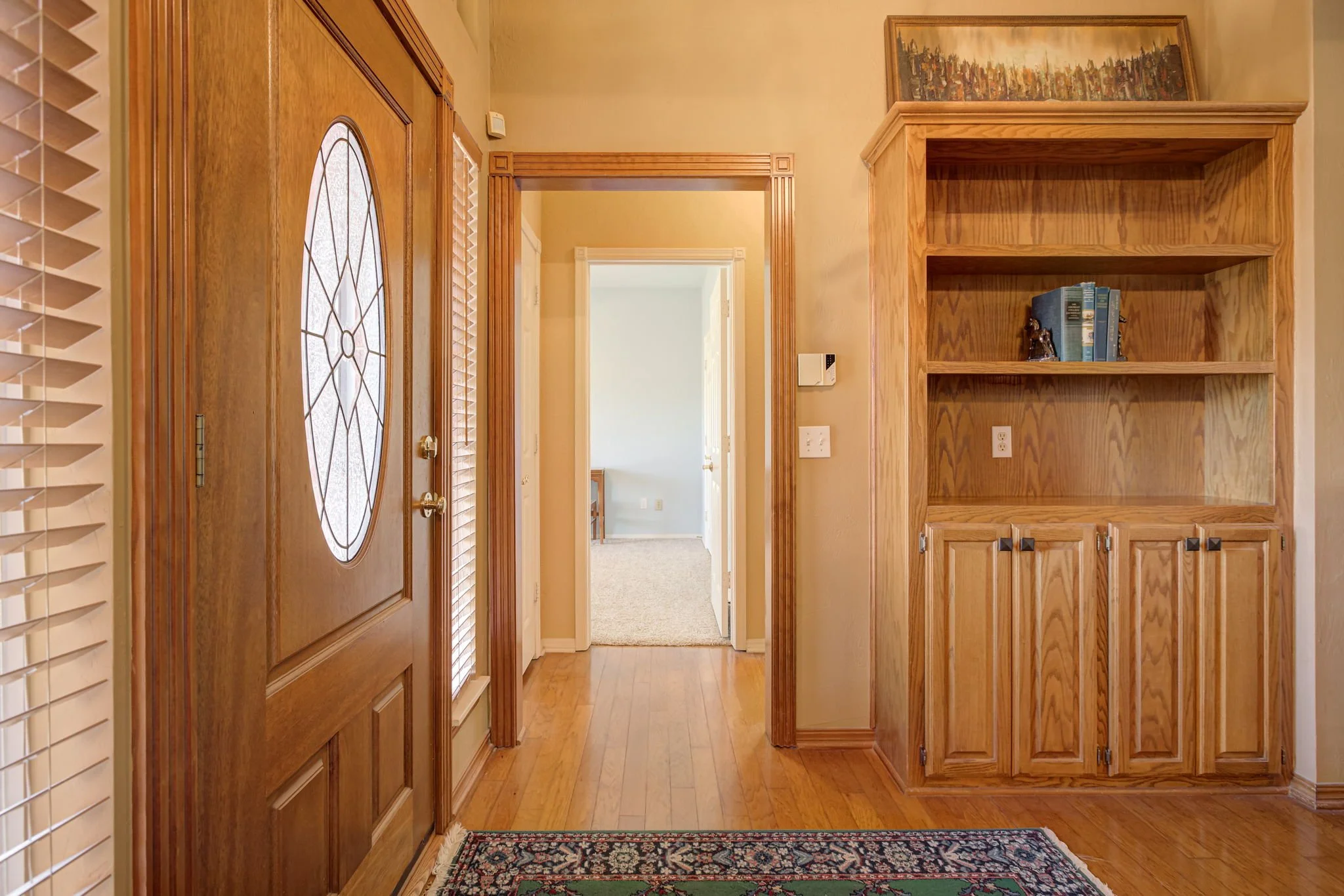 Entryway with wooden door, hardwood floors, built-in wooden bookshelf, and a small rug.