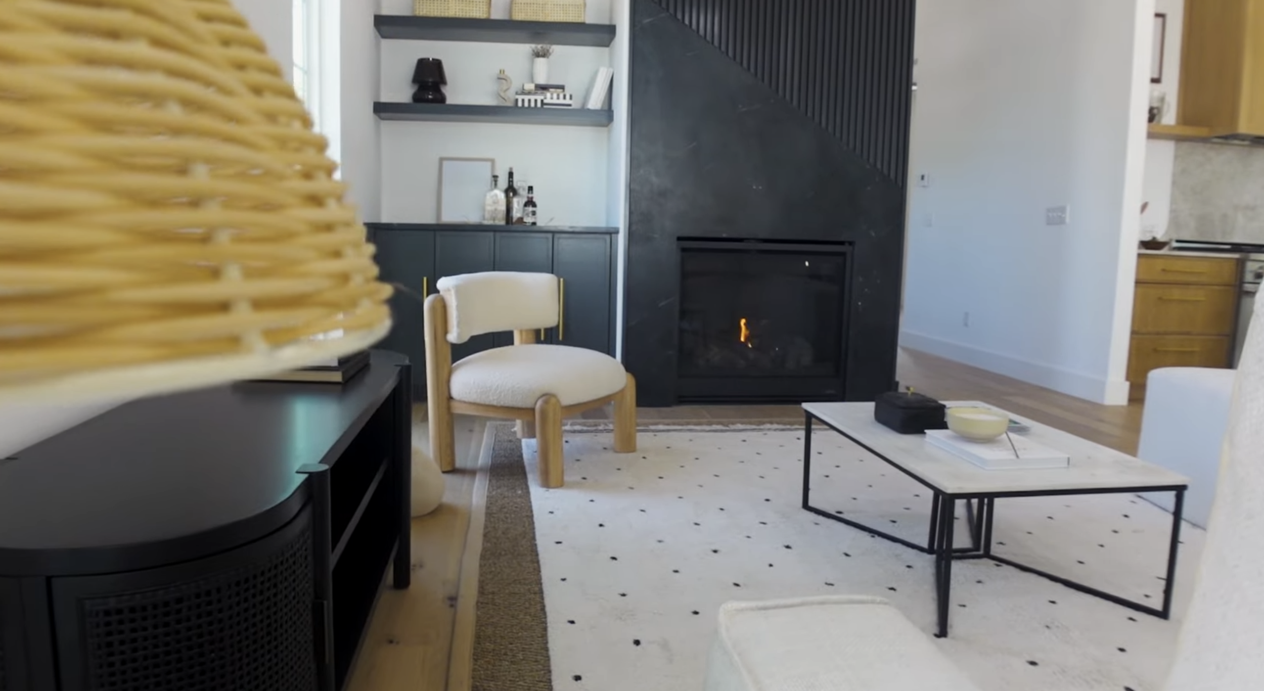 Living room with fireplace, white rug, coffee table, and chairs, with a partial view of a wicker lampshade in the foreground.