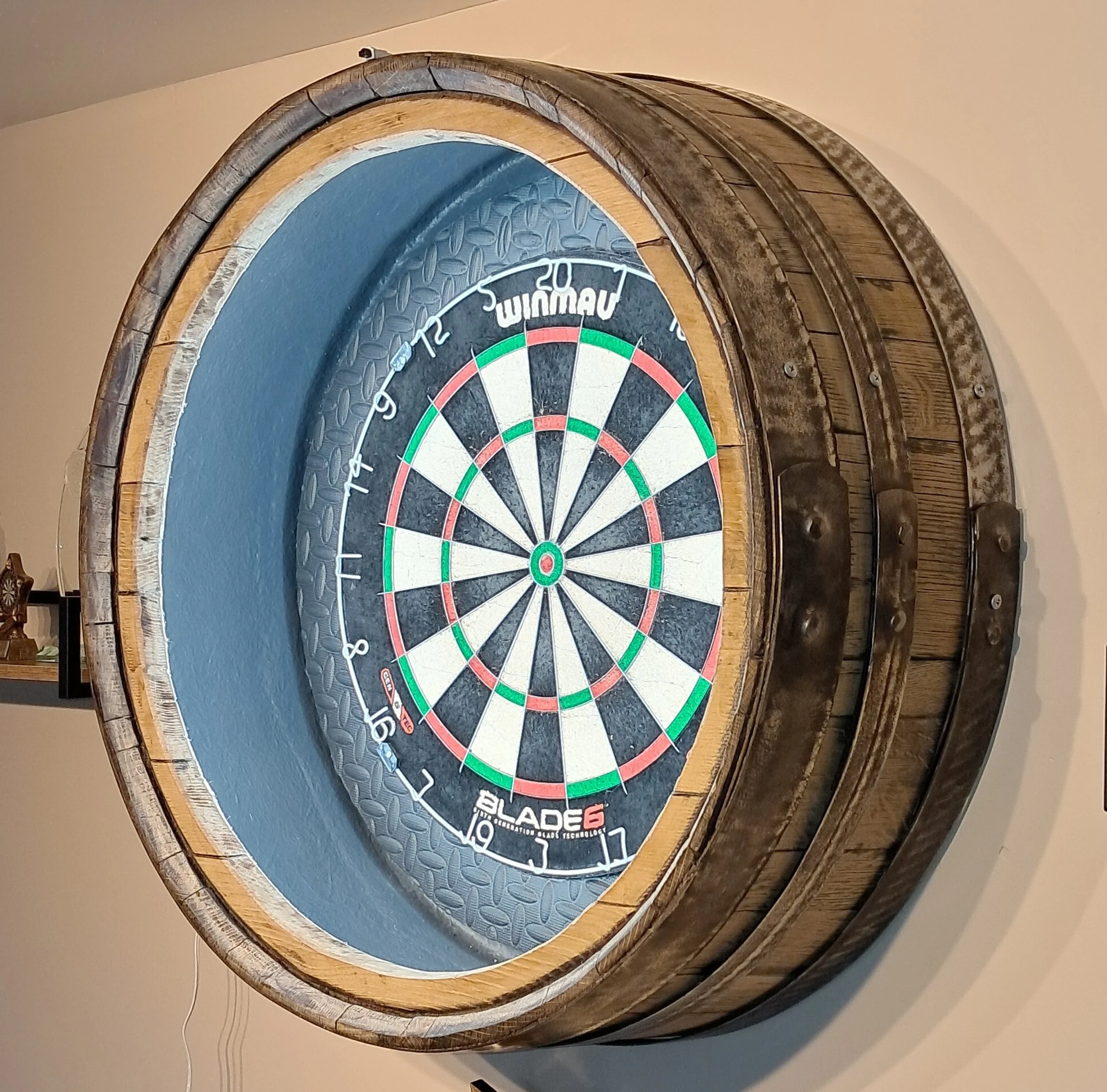 Electronic dartboard mounted on a wooden barrel-shaped wall with decorative metal bands.