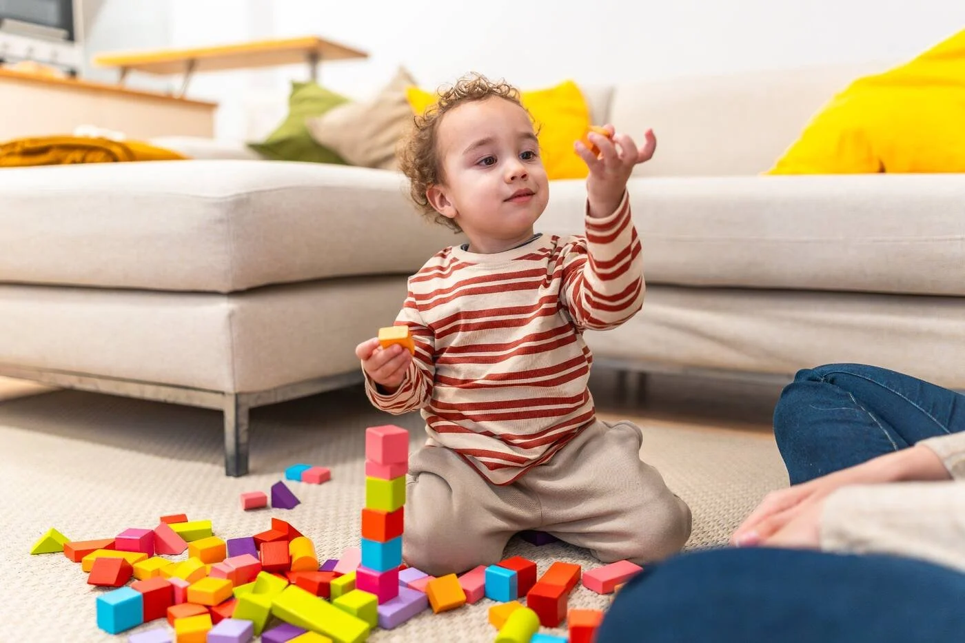 Young child building with colourful blocks at home while parent watches, representing play-based therapy for autism at Mini Minds Toronto.