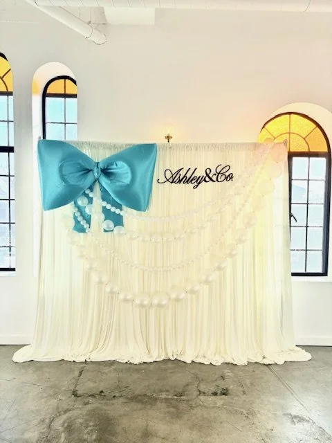 Cream drapery showcasing a giant bow and pesrl strand balloons
