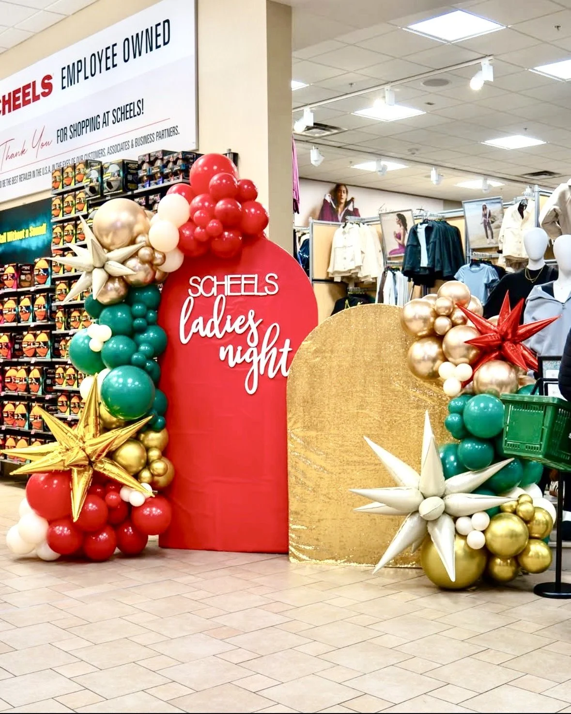 Holiday display at Scheels with balloons and stars, reading 'Ladies Night' on a red backdrop, inside a shopping mall.