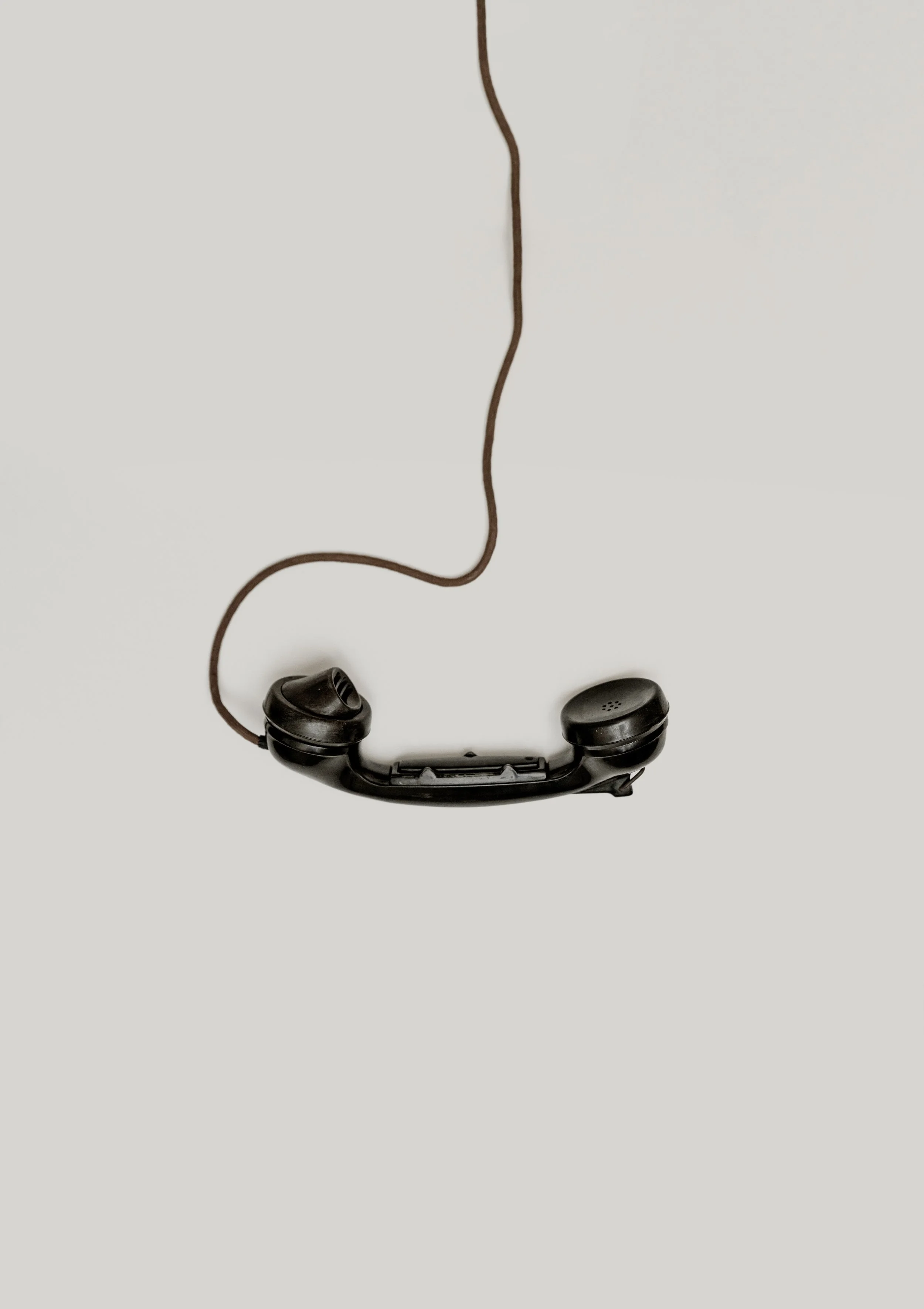 Vintage black telephone handset with a coiled cord hanging against a plain background.