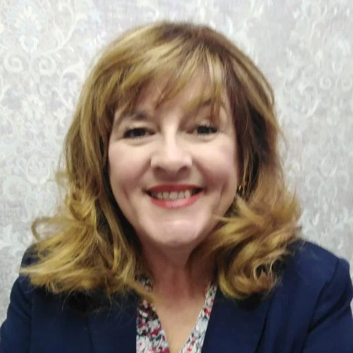 Smiling person with shoulder-length hair, wearing a dark blazer.