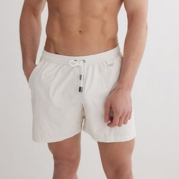 A shirtless man wearing white shorts with a drawstring, standing against a plain light background.
