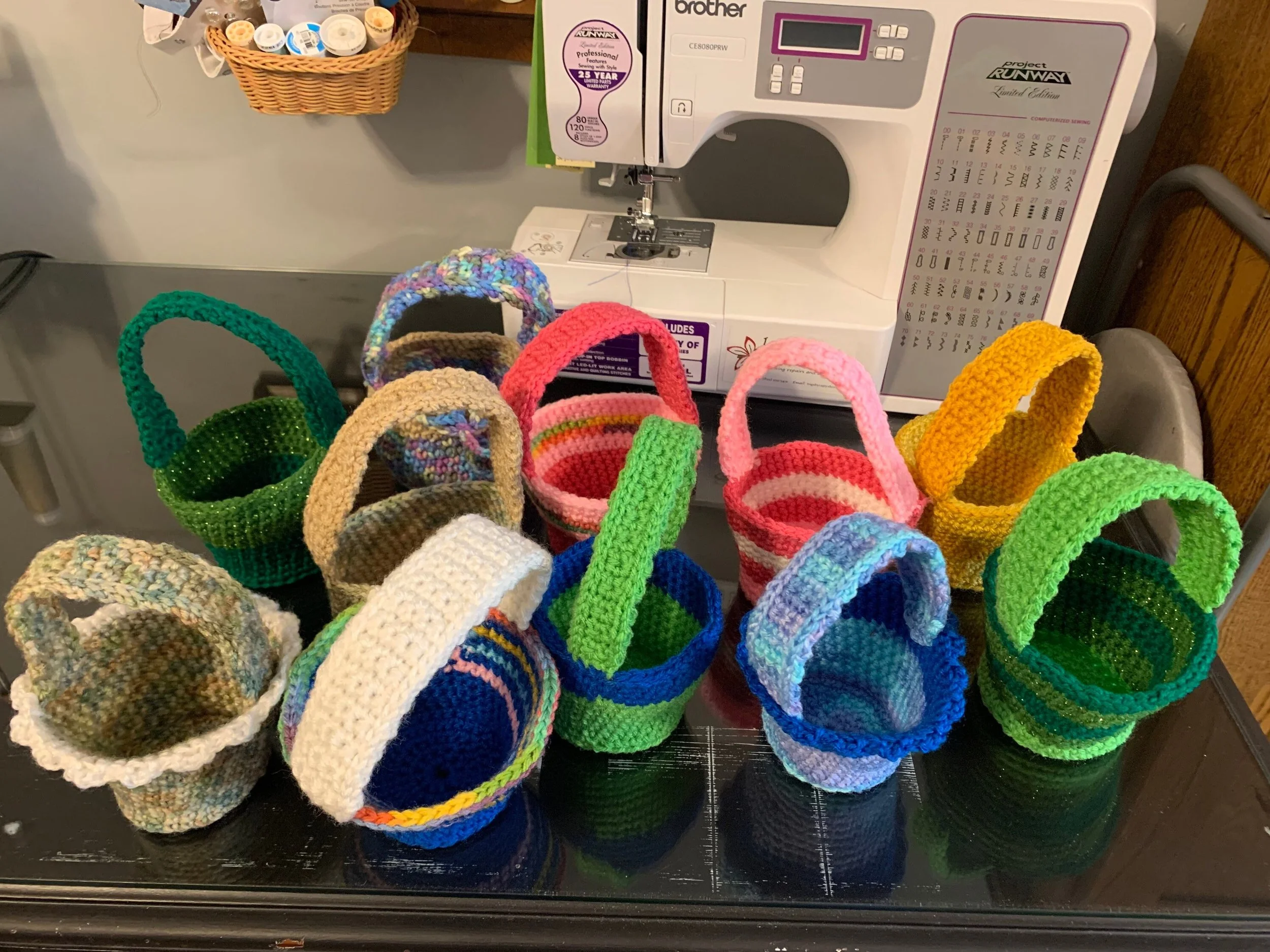 Colorful handmade crocheted baskets on a black countertop with a sewing machine in the background.