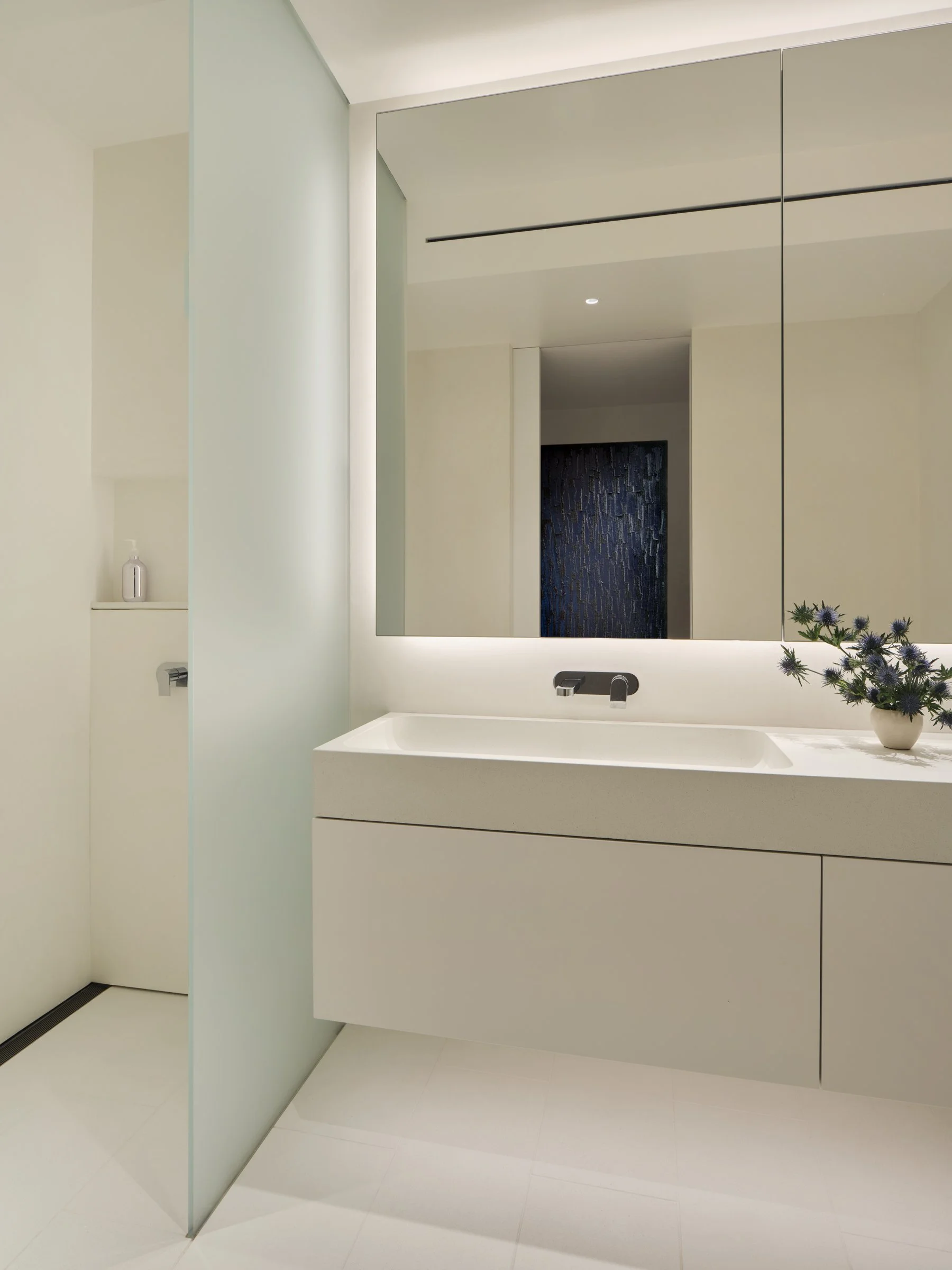 Primary bathroom with floating custom vanity, backlit mirror cabinet, frosted glass shower partition, and Ha Chong-Hyun painting reflected in the mirror — Russian Hill San Francisco interior design by Studio Collins Weir