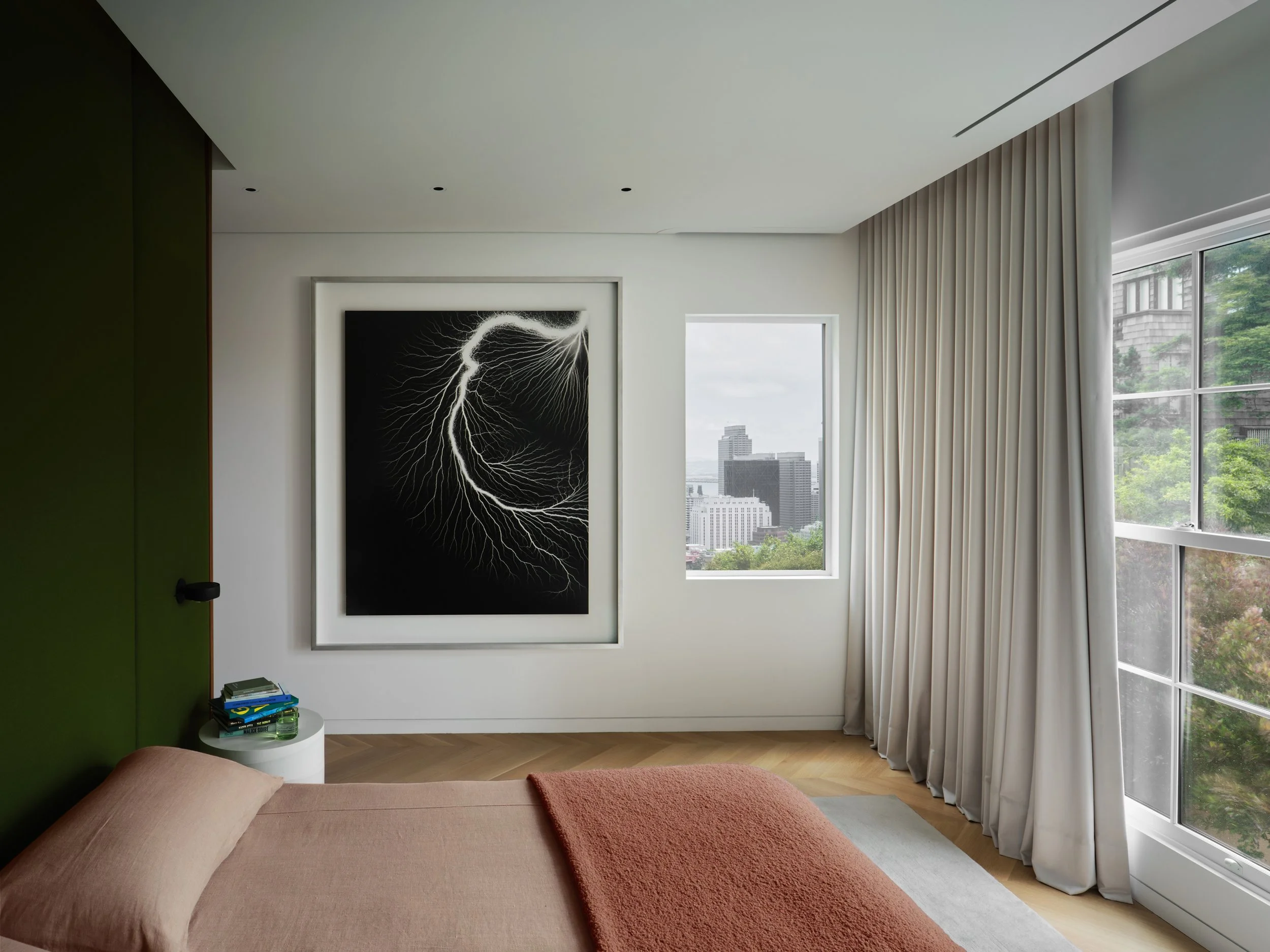 Secondary bedroom with Hiroshi Sugimoto lightning photograph, San Francisco skyline views through picture window, and moss green upholstered headboard — Russian Hill interior design by Studio Collins Weir