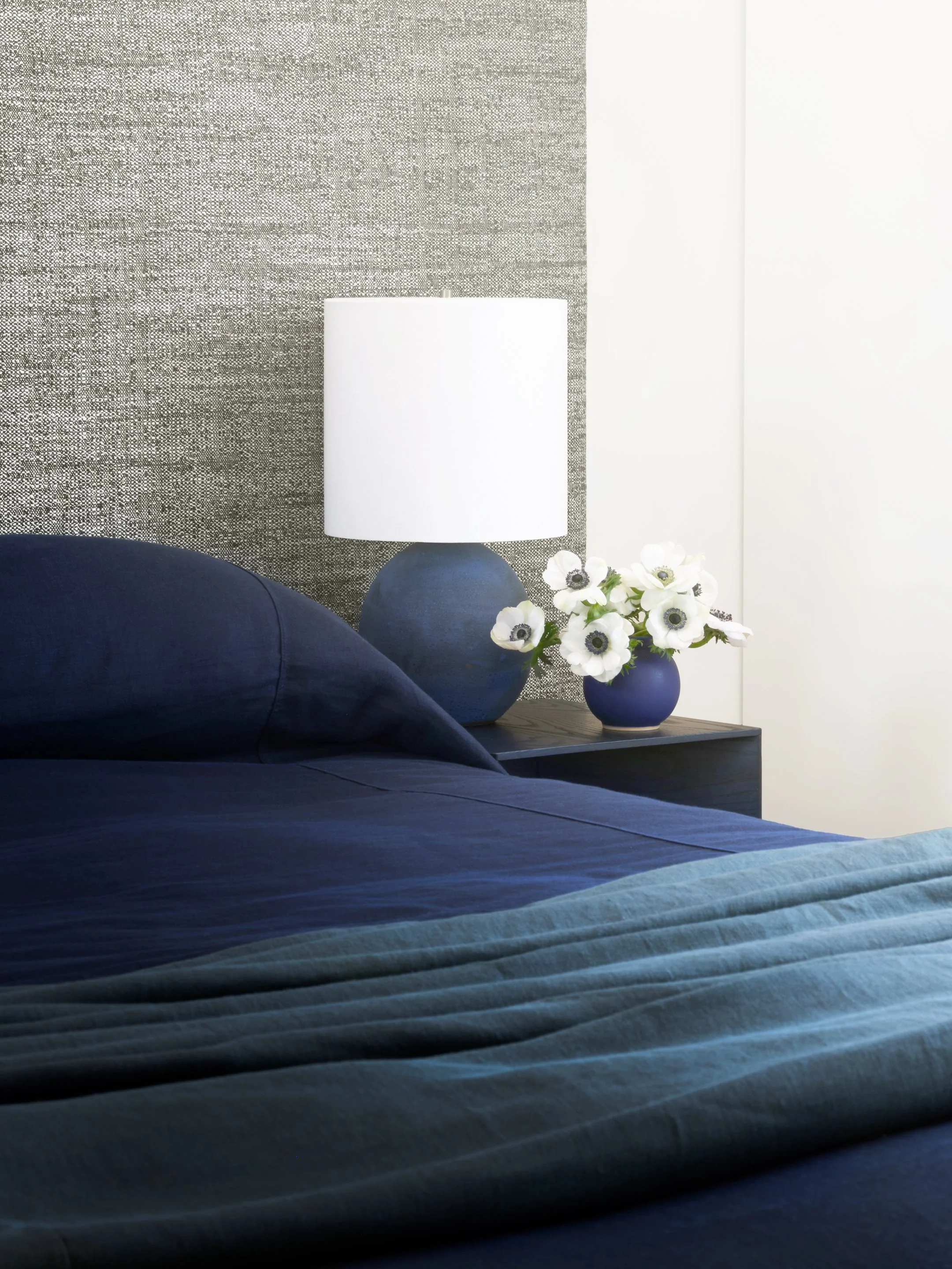 Modern bedroom with blue textiles, ceramic table lamp, and styled nightstand detail