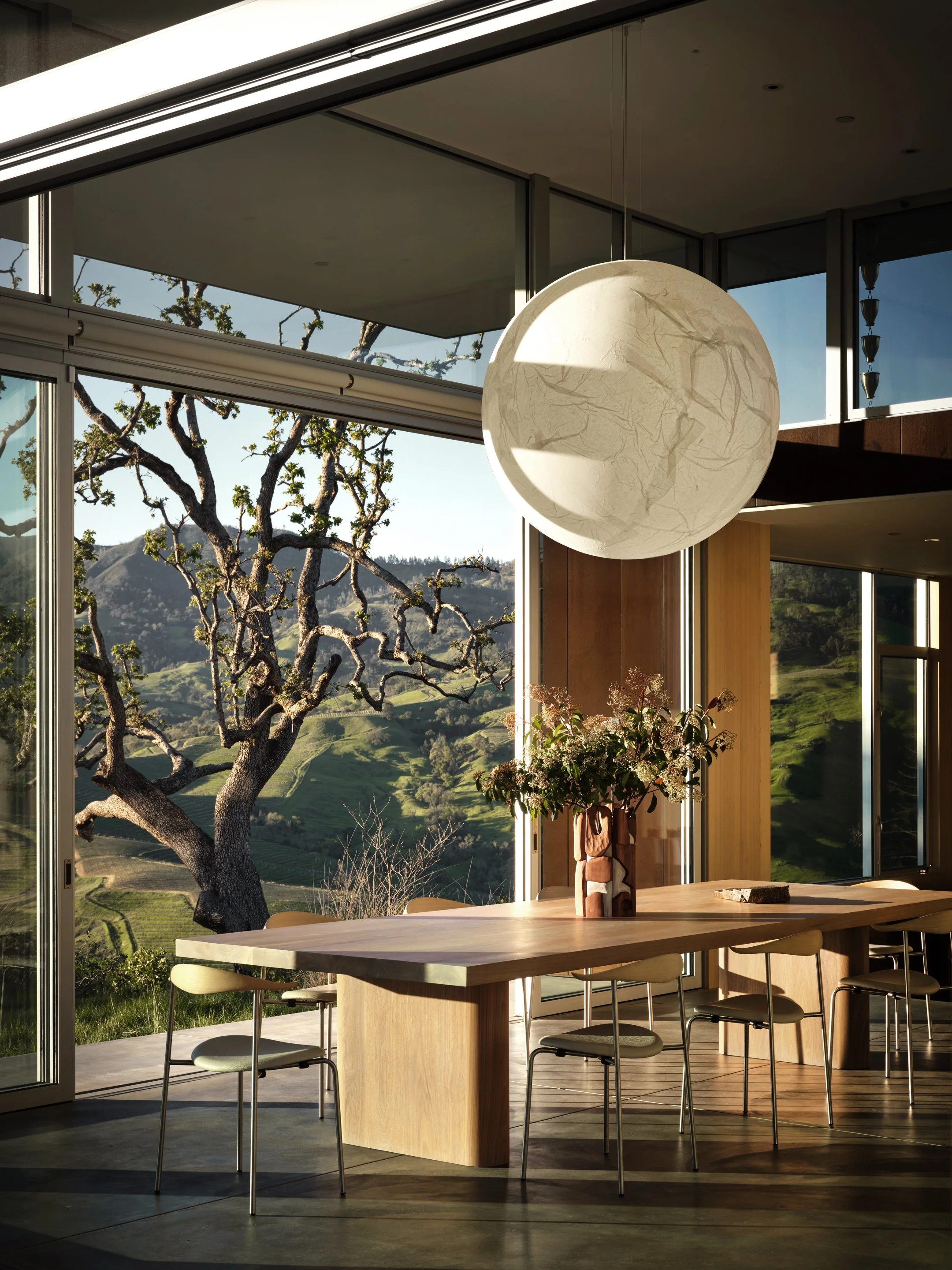 Modern dining room with floor to ceiling windows, custom wood table, and panoramic landscape views