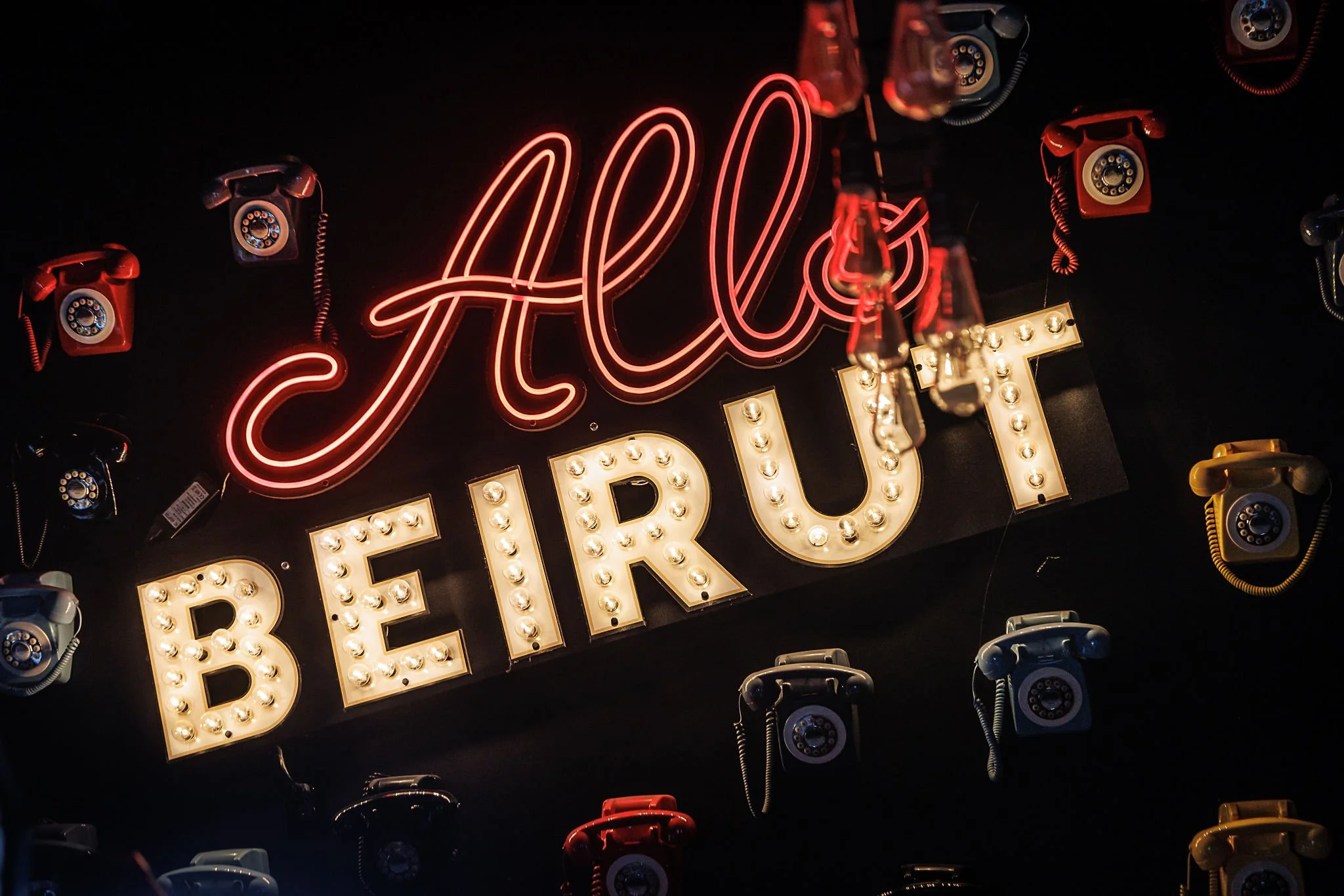 Neon sign with the words 'Hello' in red cursive and 'BEIRUT' in bold letters surrounded by vintage rotary dial telephones in various colors.