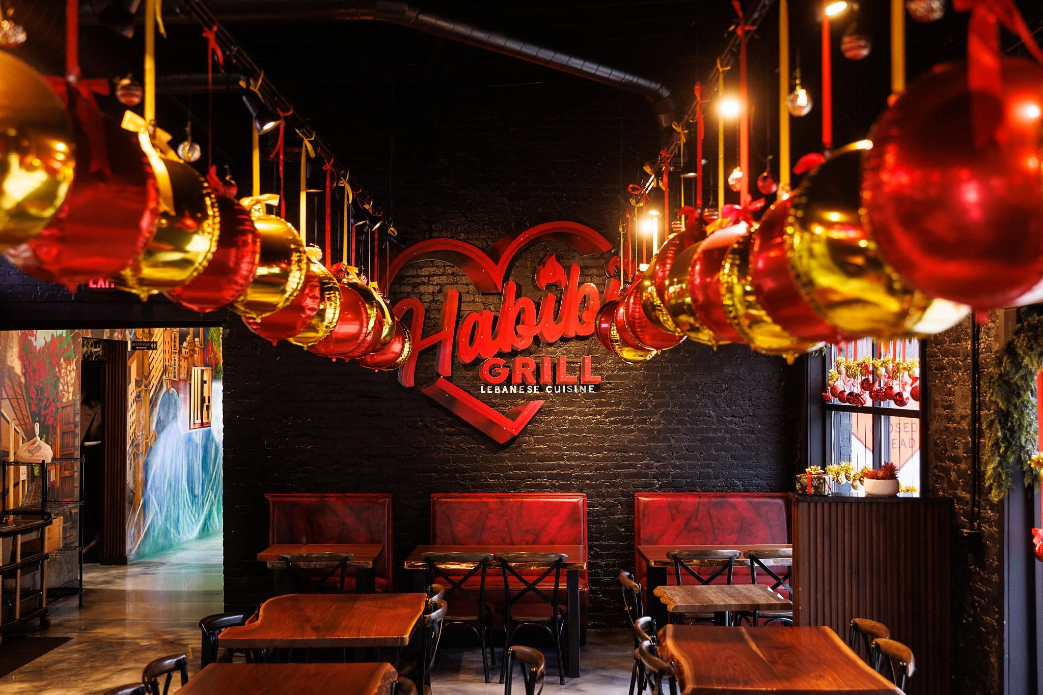 Interior of Habibi Grill Lebanese Cuisine restaurant with red and gold hanging Christmas ornaments, a black brick wall, and red seating.