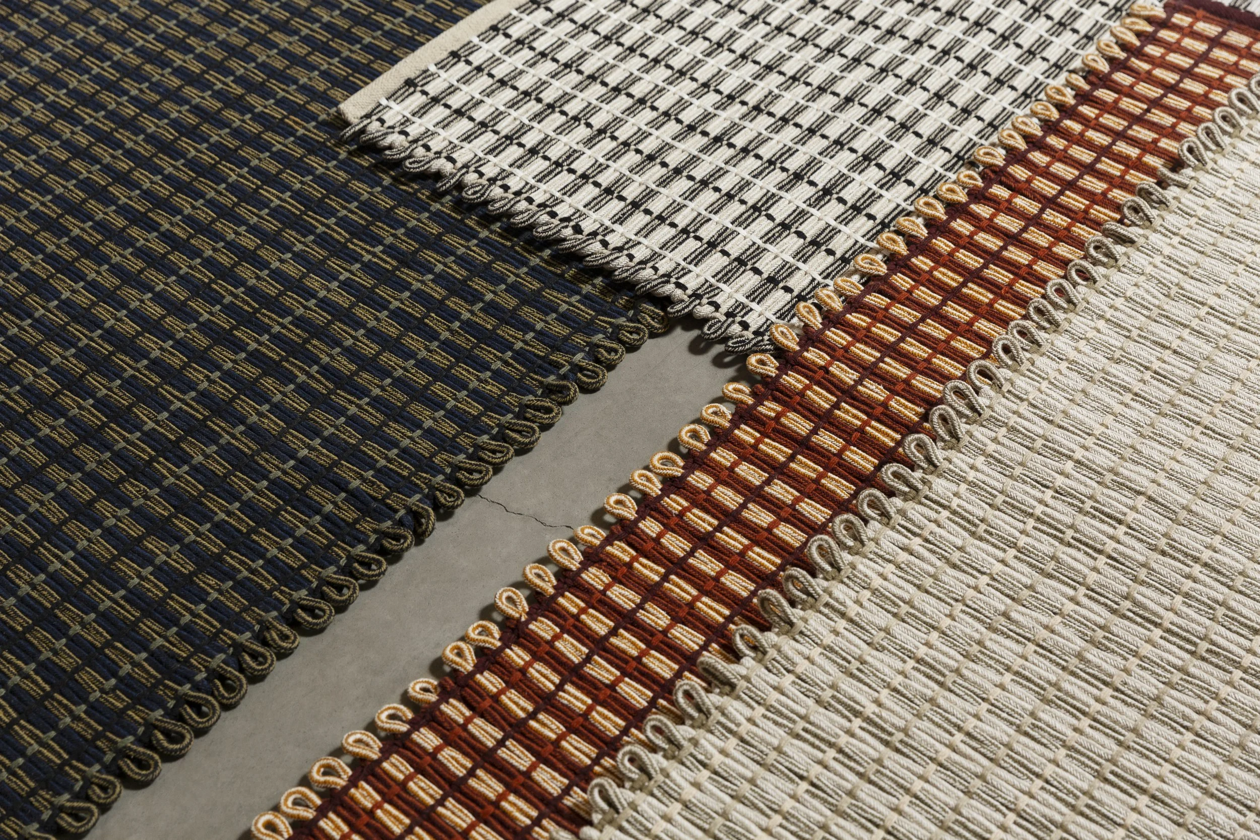 Close-up view of four woven fabric swatches with different thread patterns and colors, including dark blue, gray, red, and beige.
