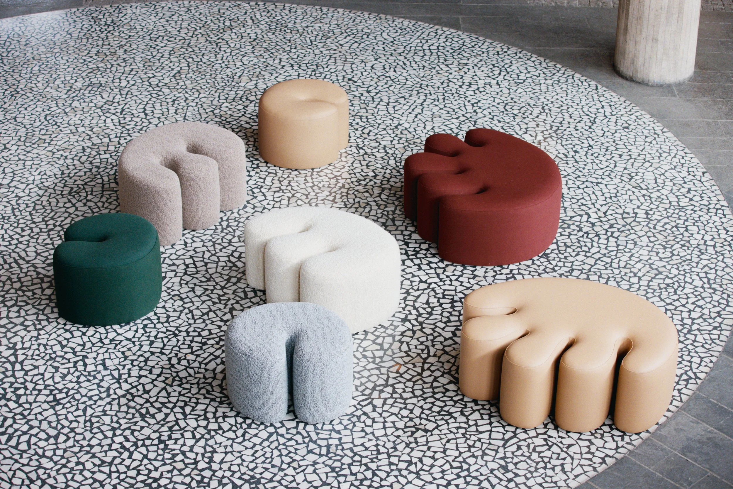 Colorful, rounded, and textured seating stools arranged in a semi-circle on a mosaic tile floor with geometric pattern.