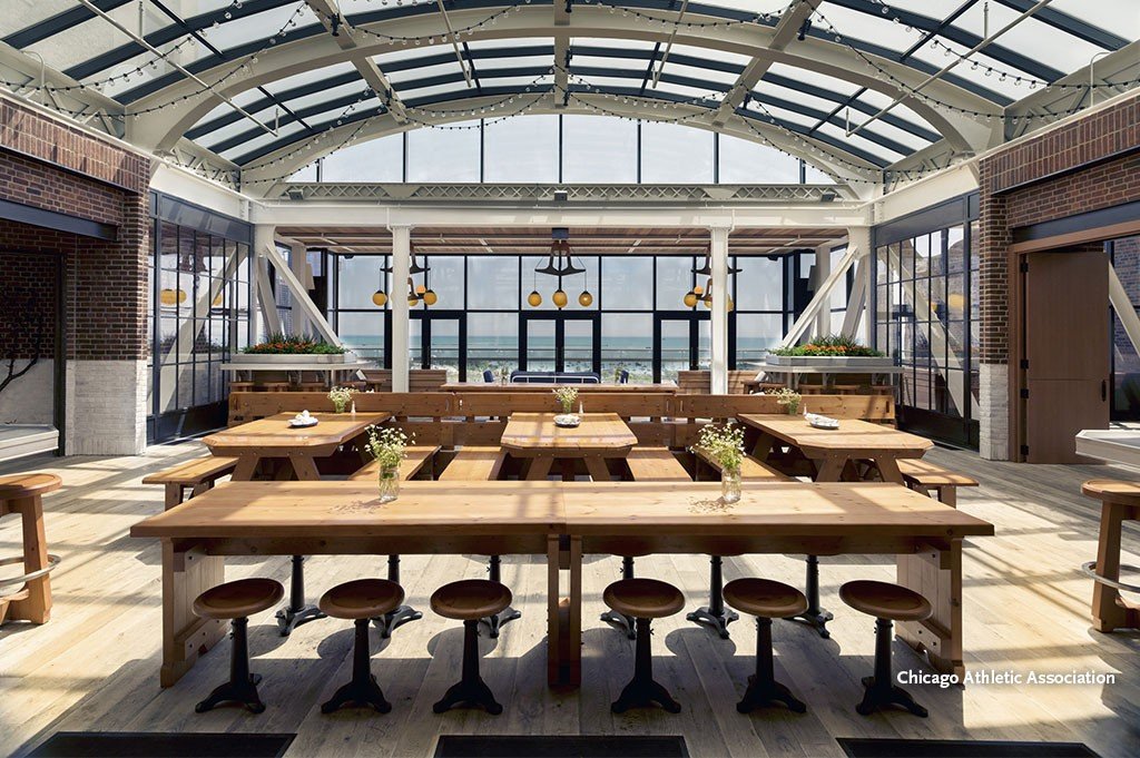 Interior of a bright restaurant or cafe with wooden tables and chairs, large glass windows, and a glass ceiling, with view of the outside.