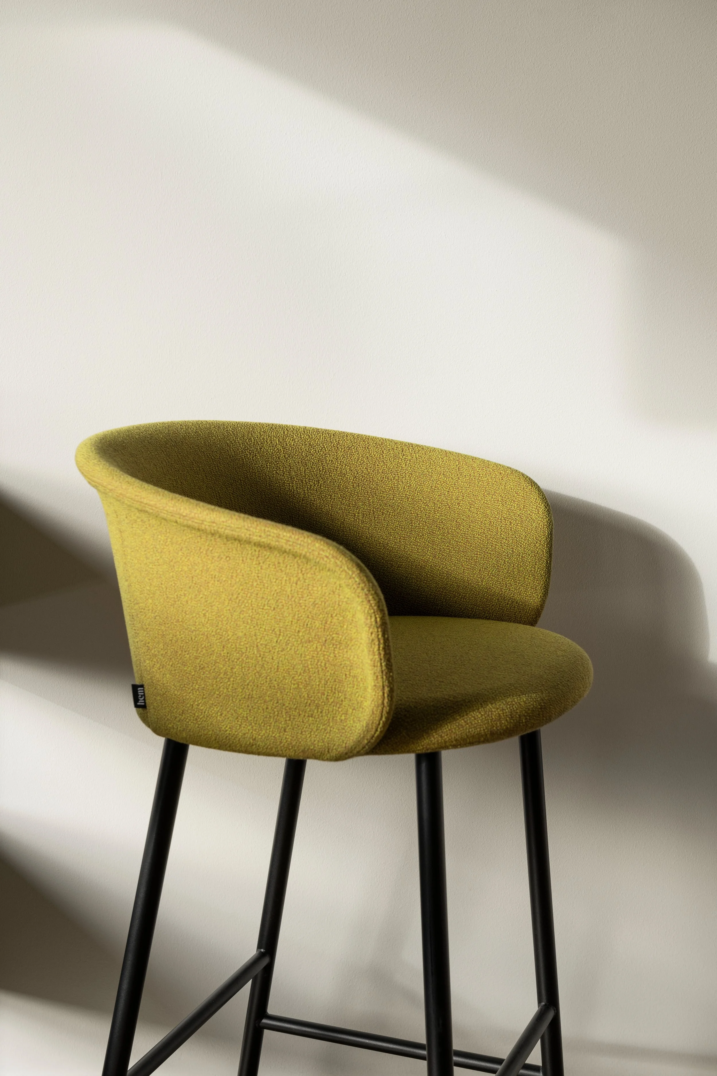 A mustard yellow upholstered chair with black wooden legs, placed against a plain white wall with shadows.
