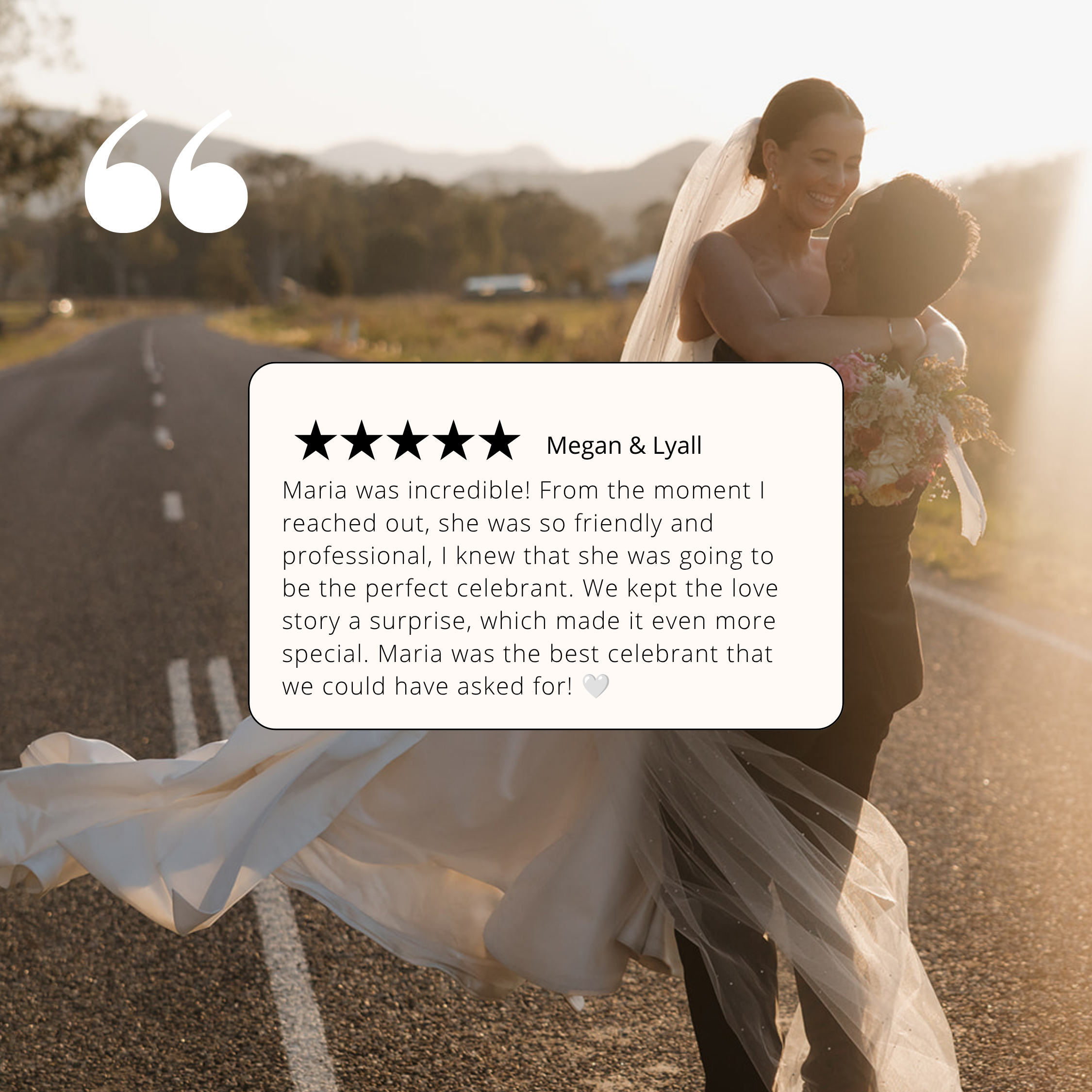 A bride in a wedding dress and veil hugging a woman, standing outdoors on a road with mountains and trees in the background during sunset.