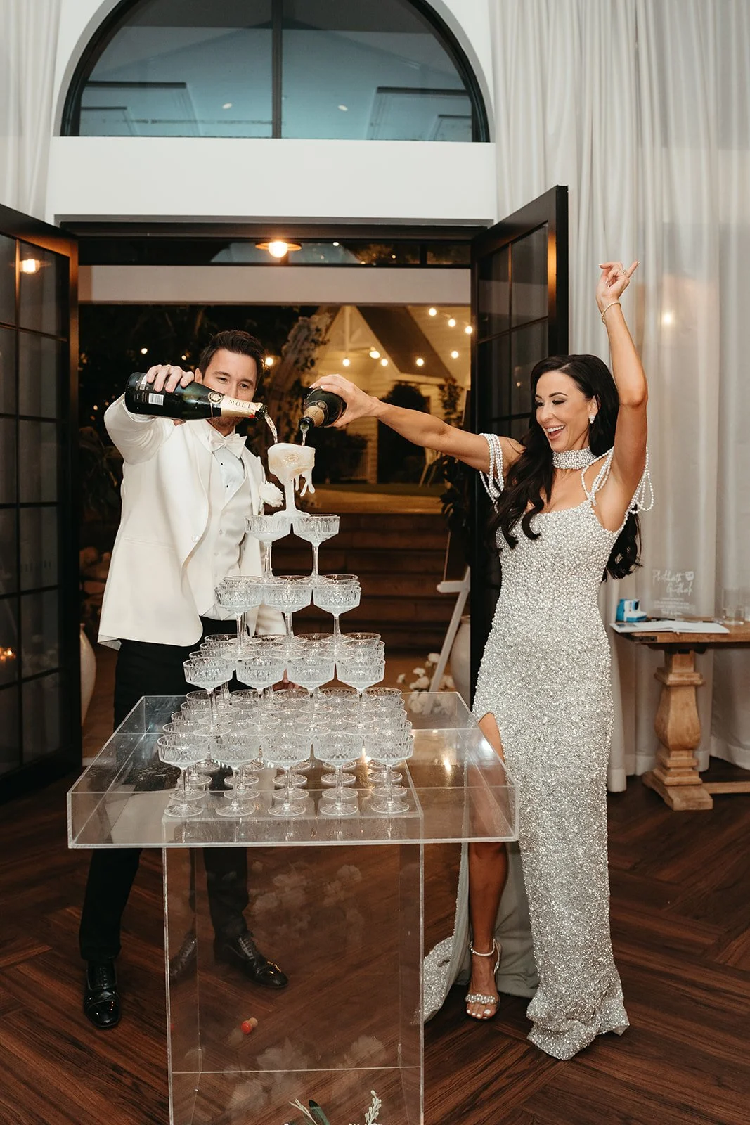 A wedding celebration where a bride and groom are pouring champagne into a pyramid of glasses.